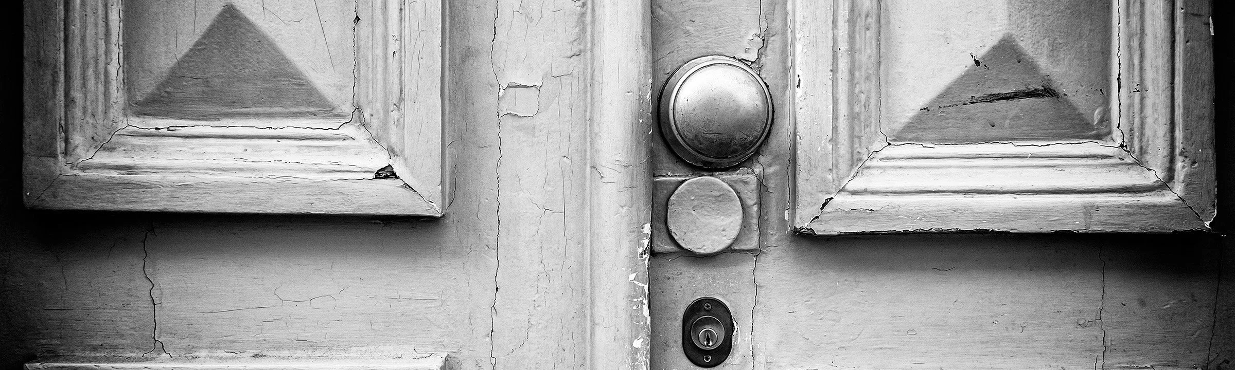 Close-up black-and-white photograph of a weathered door and round doorknob.