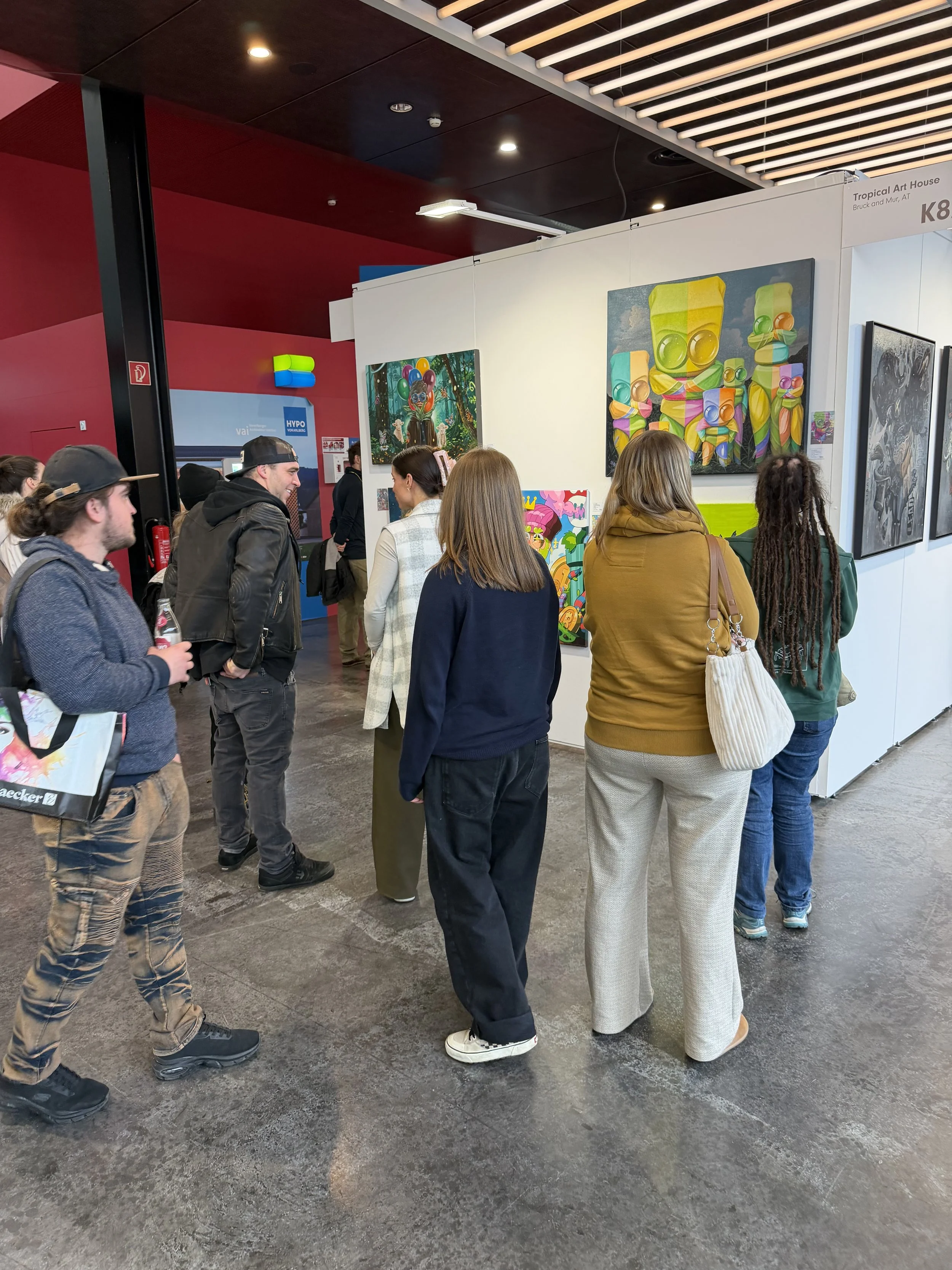 People viewing colorful modern art paintings at an art exhibition.
