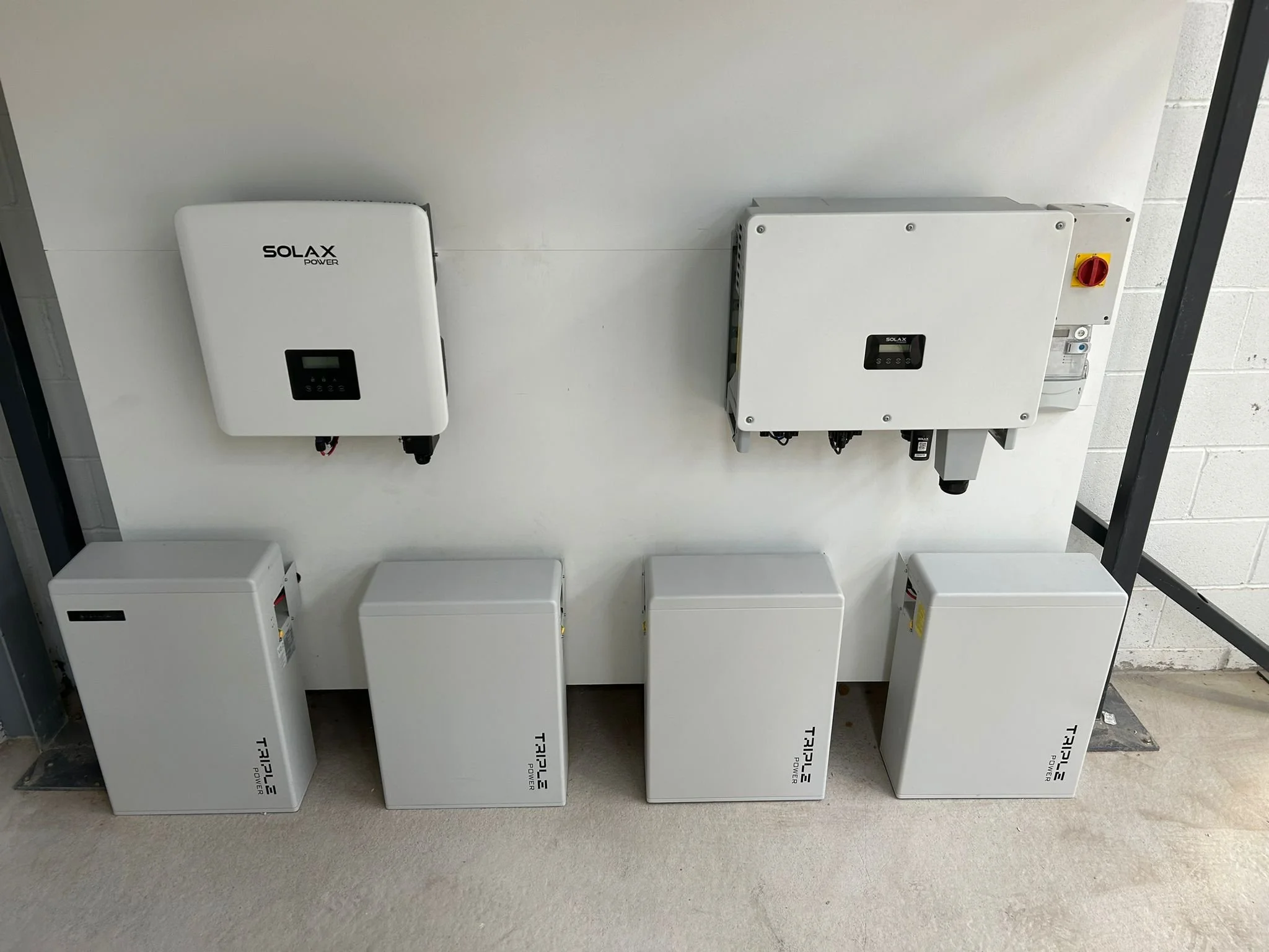 Outdoor solar panel setup with a portable power station on green grass, glass solar panels arranged in rows, and hills with trees in the background under cloudy sky.