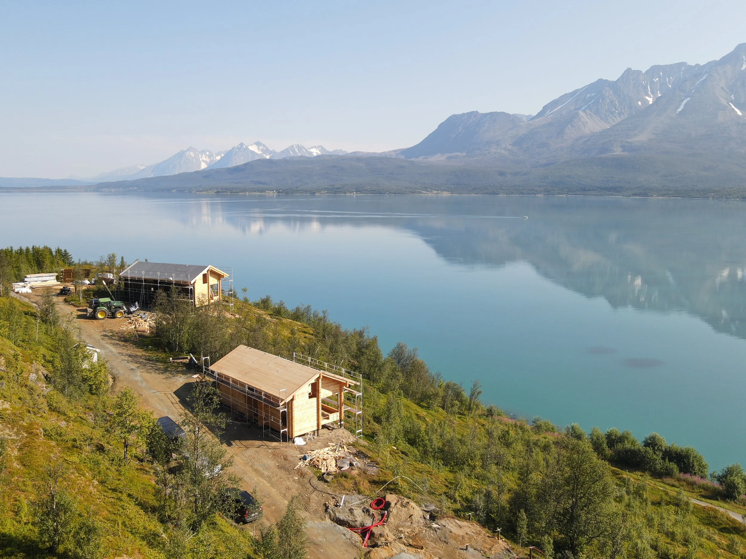 Construction of wooden houses on a hillside overlooking a large lake with mountains in the background.
