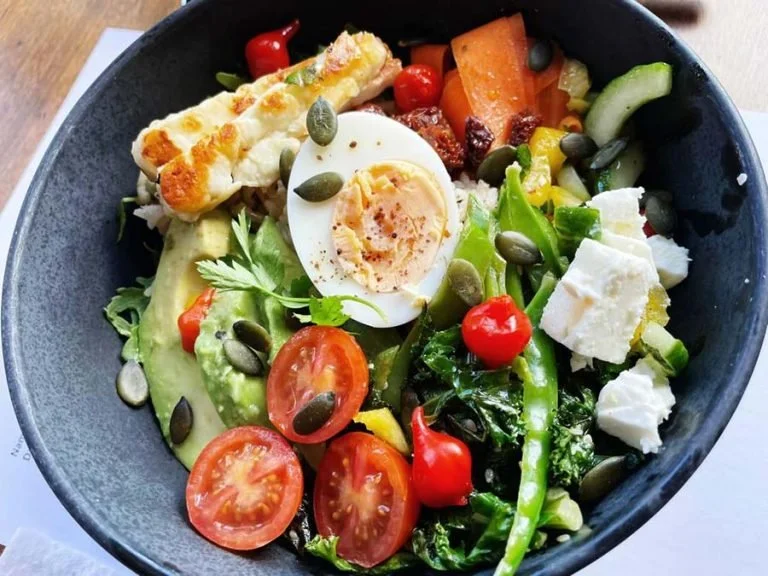 A bowl of salad with cherry tomatoes, boiled egg, avocado, greens, pumpkin seeds, cheese, and grilled chicken.