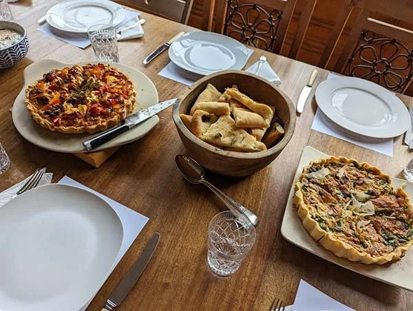 Pizza, breadsticks, and a second pizza on a dining table set with white plates and utensils.