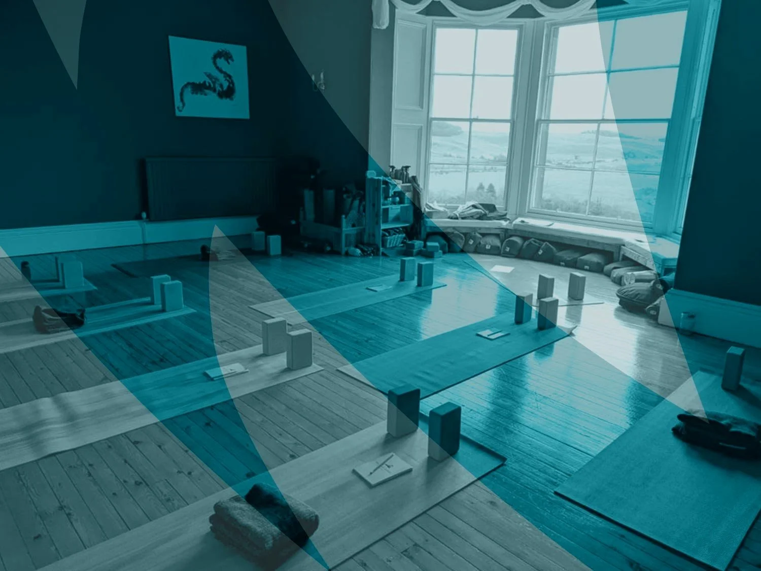 A cozy yoga studio with wooden floors, yoga mats, and blocks arranged on the floor near a large window overlooking a scenic landscape.
