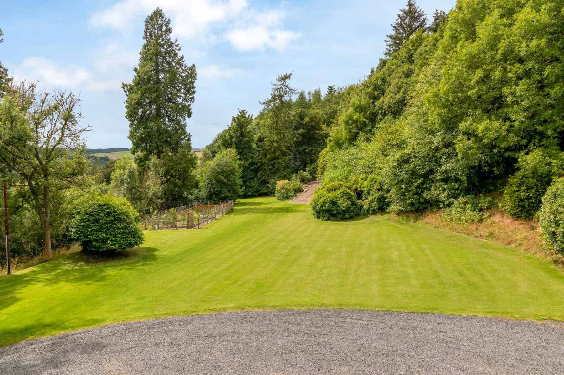 A lush green outdoor area with a well-maintained lawn bordered by trees and bushes, under a partly cloudy sky.