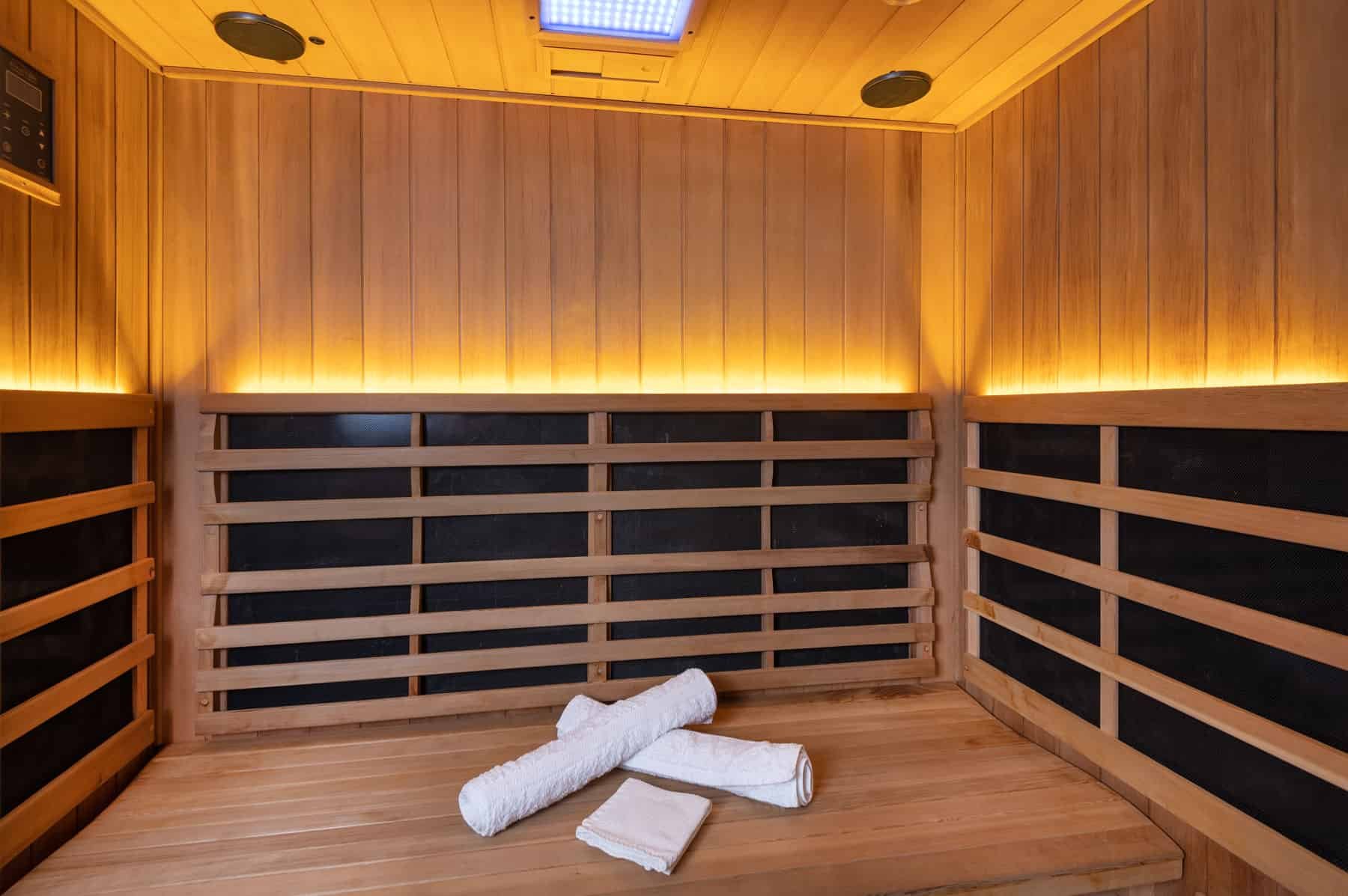 Interior of a wooden sauna room with benches, rolled white towels, and soft lighting along the wall.