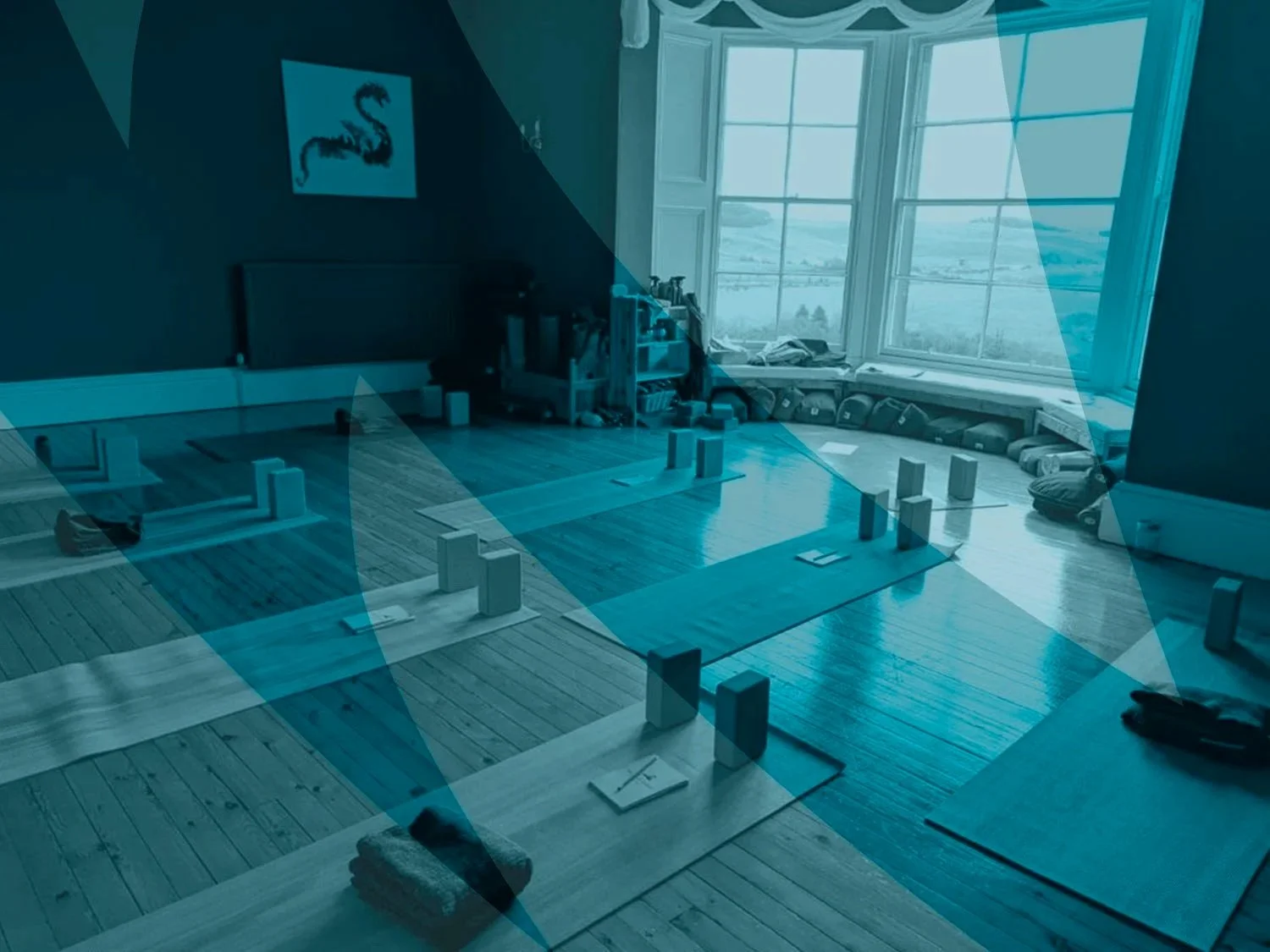 A cozy yoga studio with wooden floors, yoga mats, and blocks arranged on the floor near a large window overlooking a scenic landscape.