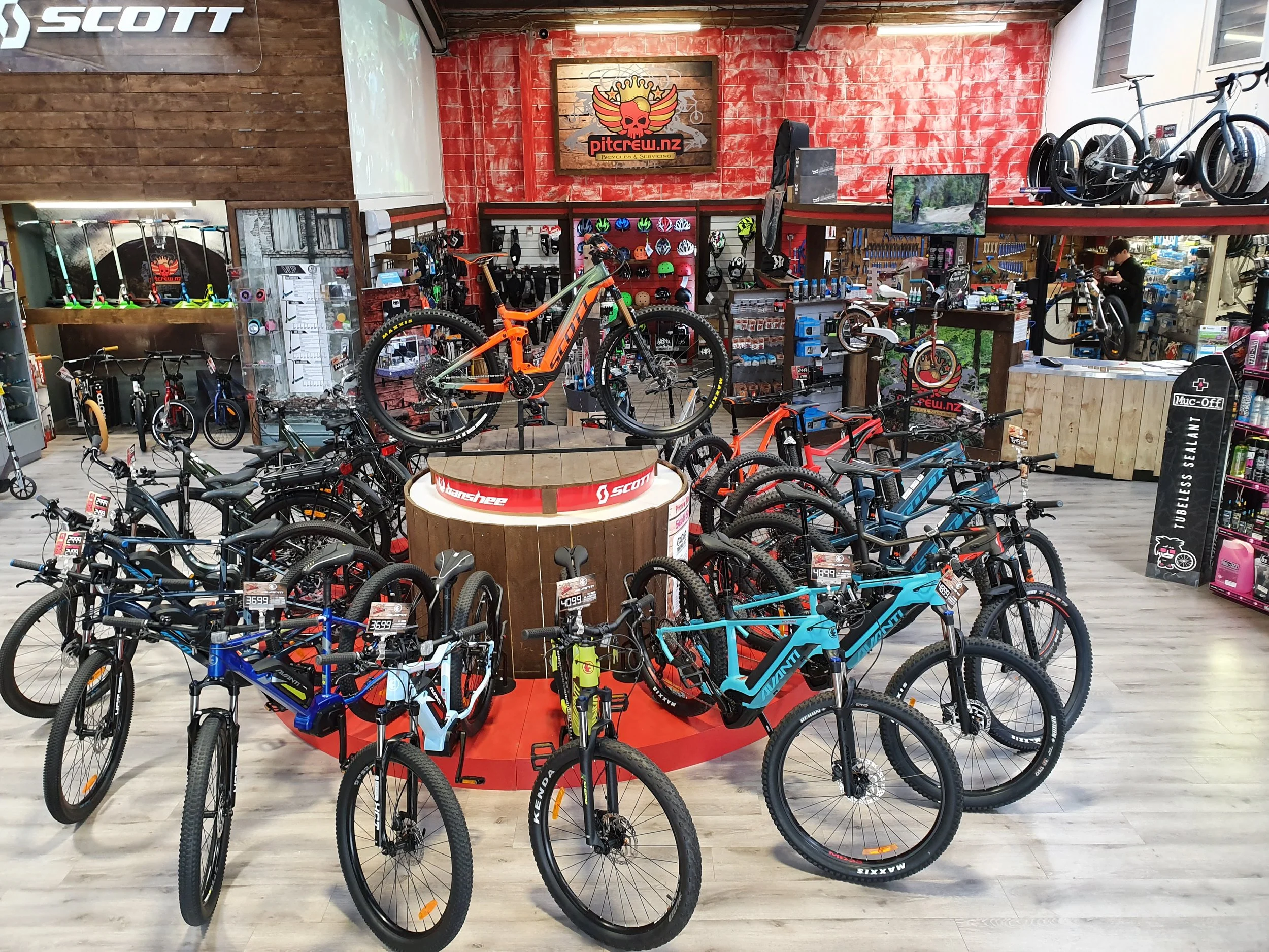A bike shop displaying various mountain bikes, helmets, and cycling accessories on shelves and walls, with a red and wood-themed interior.