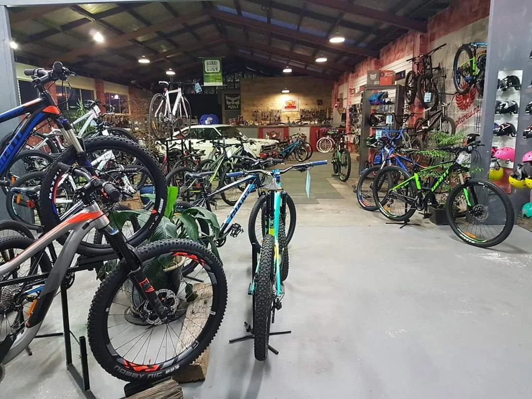 Indoor bike shop with various mountain and road bikes on display, including helmets on a wall to the right, and a workbench in the back.