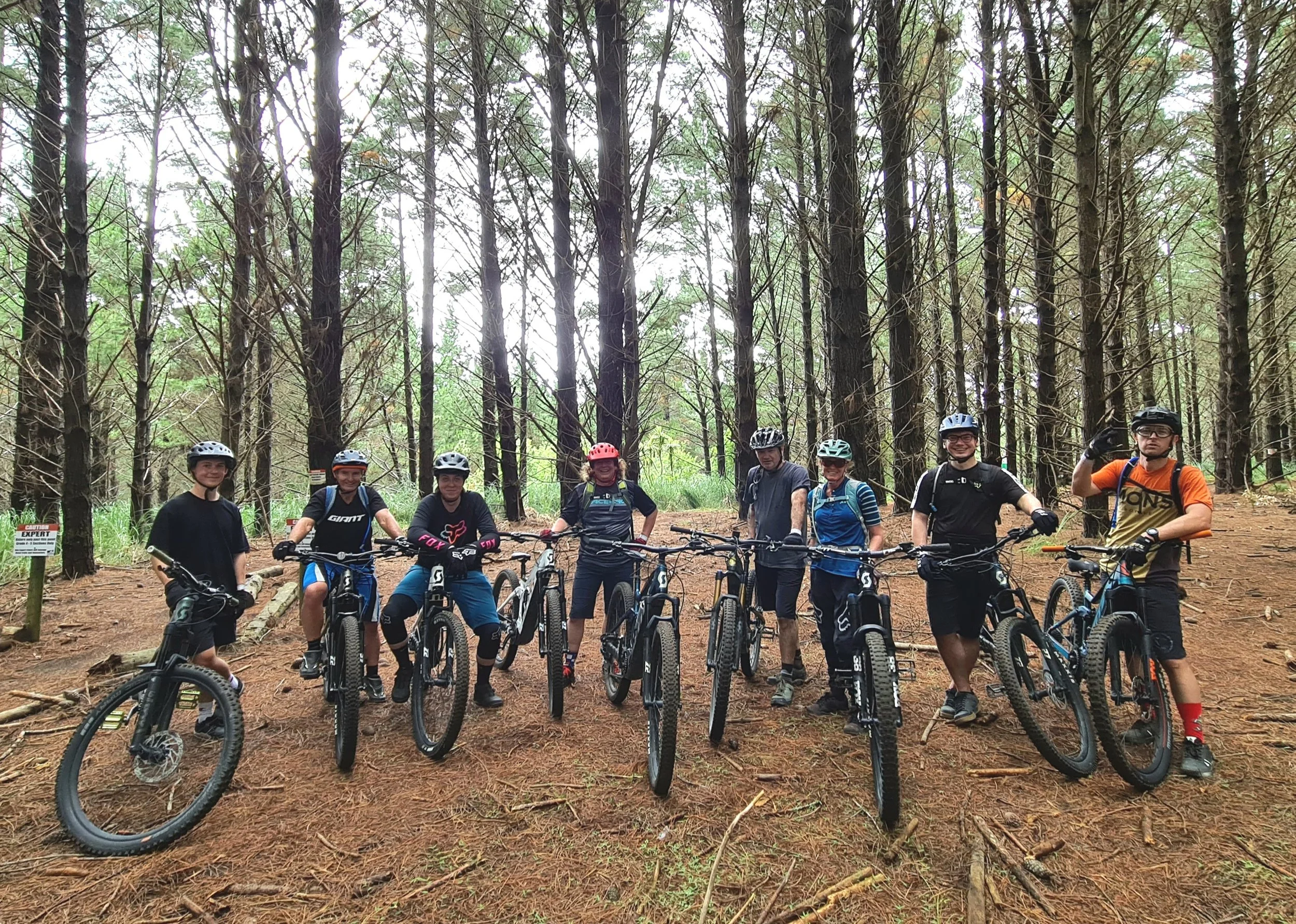 Group of mountain bikers in helmets standing with bikes in a wooded forest.