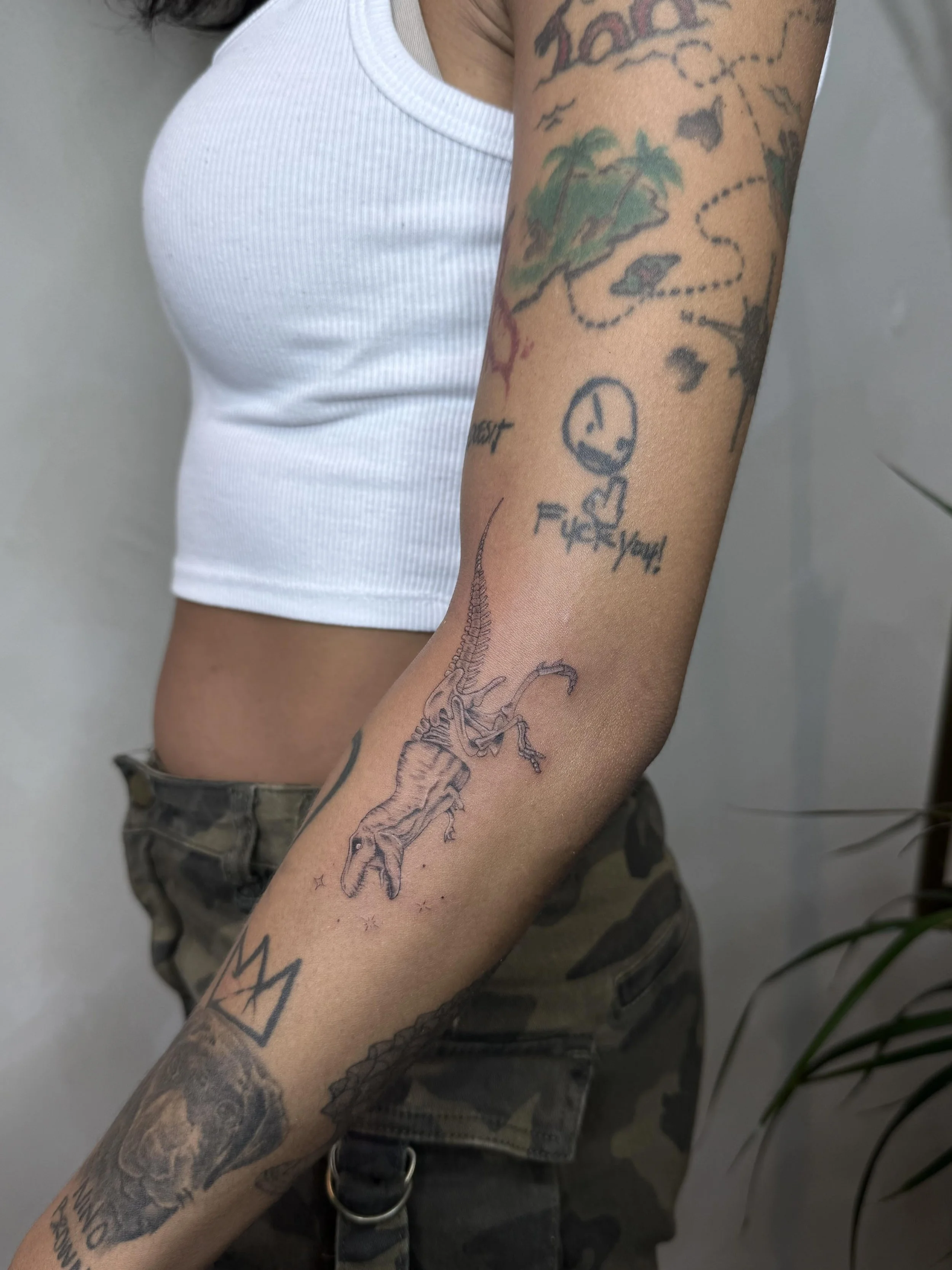 Fine-line T-rex dinosaur tattoo with delicate skeletal detailing along the forearm, by Priscilla Shafighi.