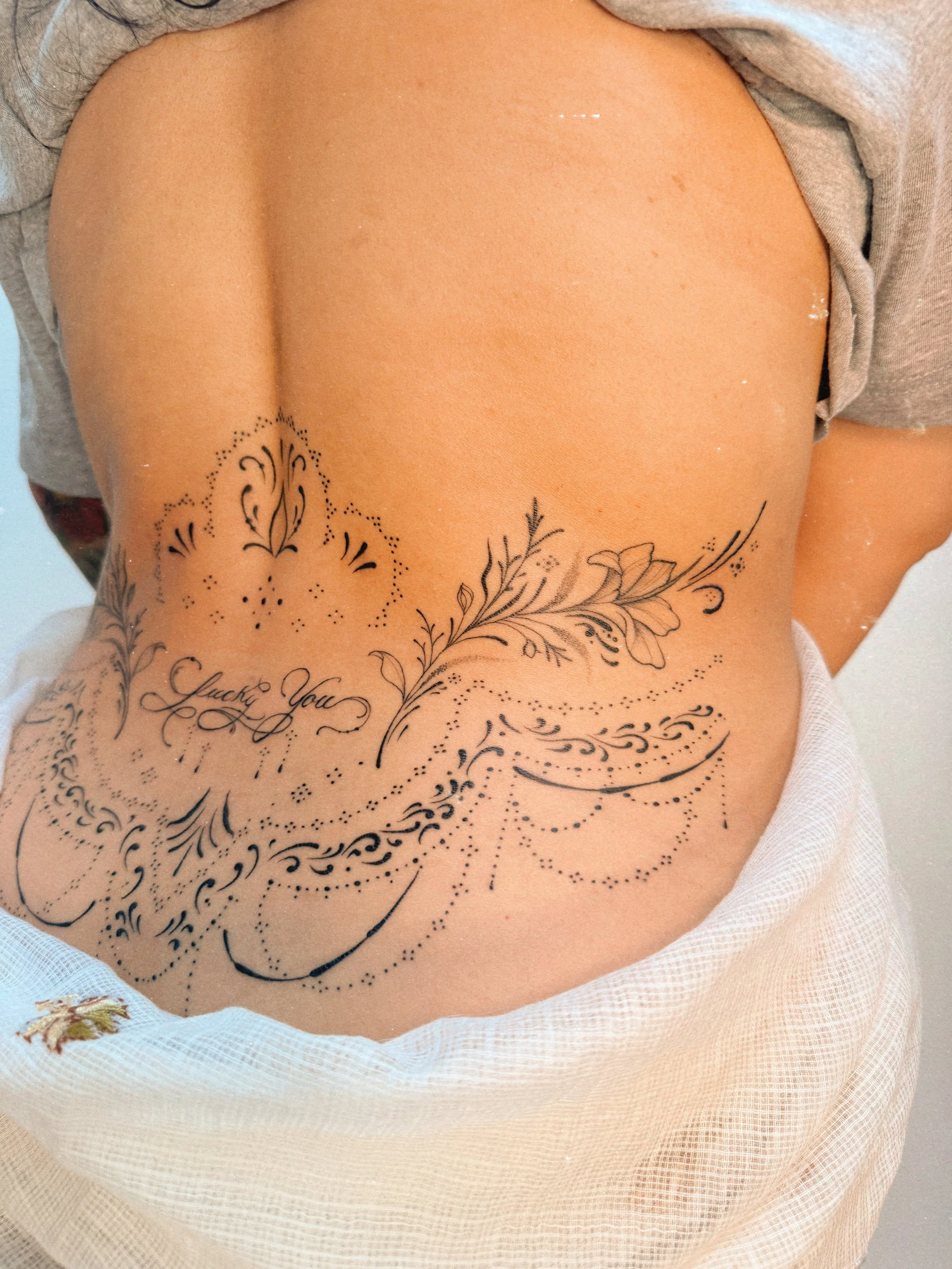 Fine line ornamental side tattoo by Ámya Mila featuring floral linework, decorative dotwork, and flowing botanical details across the ribs and waist.