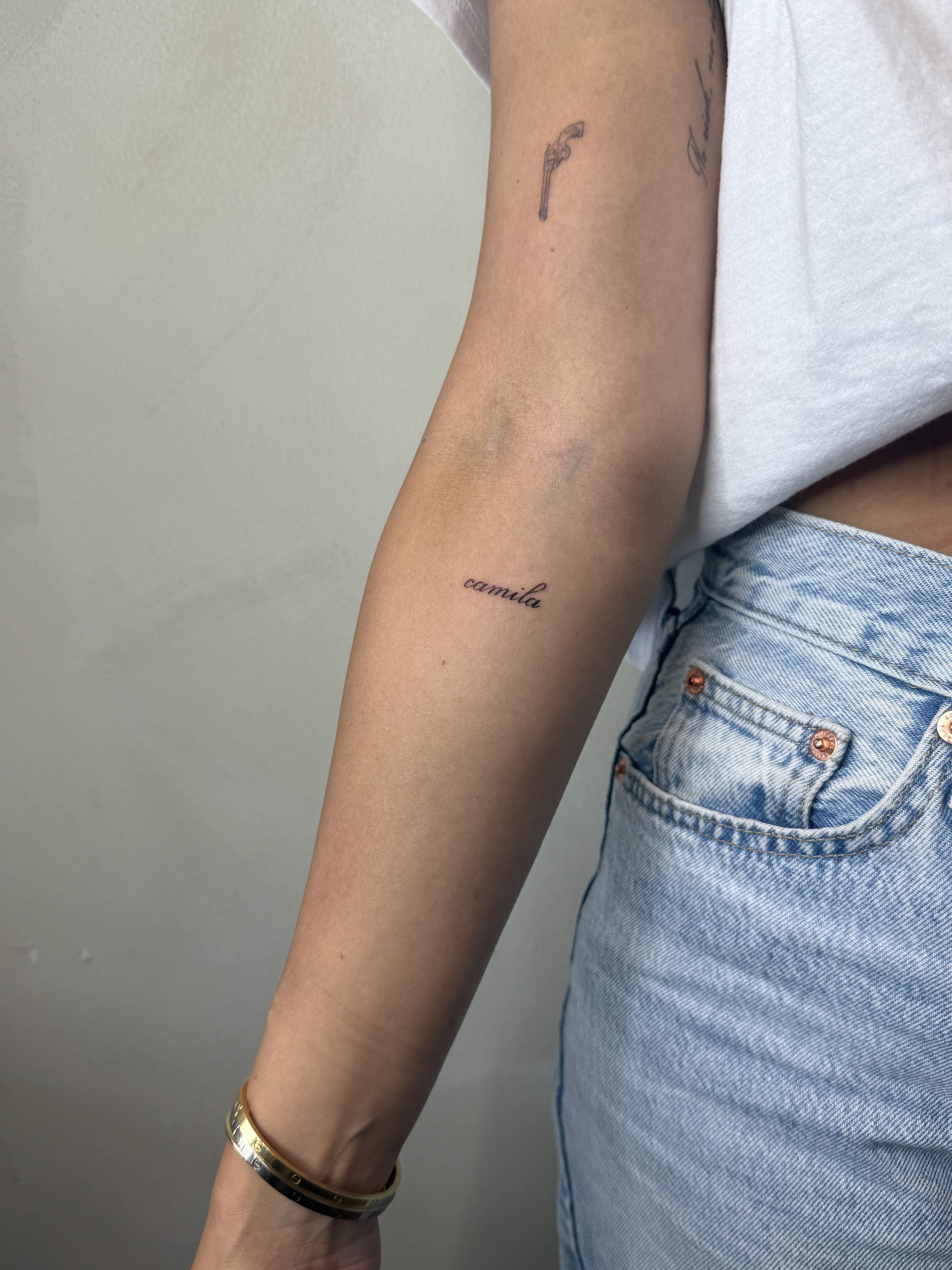 Fine-line script tattoo reading “camila” on the inner forearm, by Priscilla Shafighi.