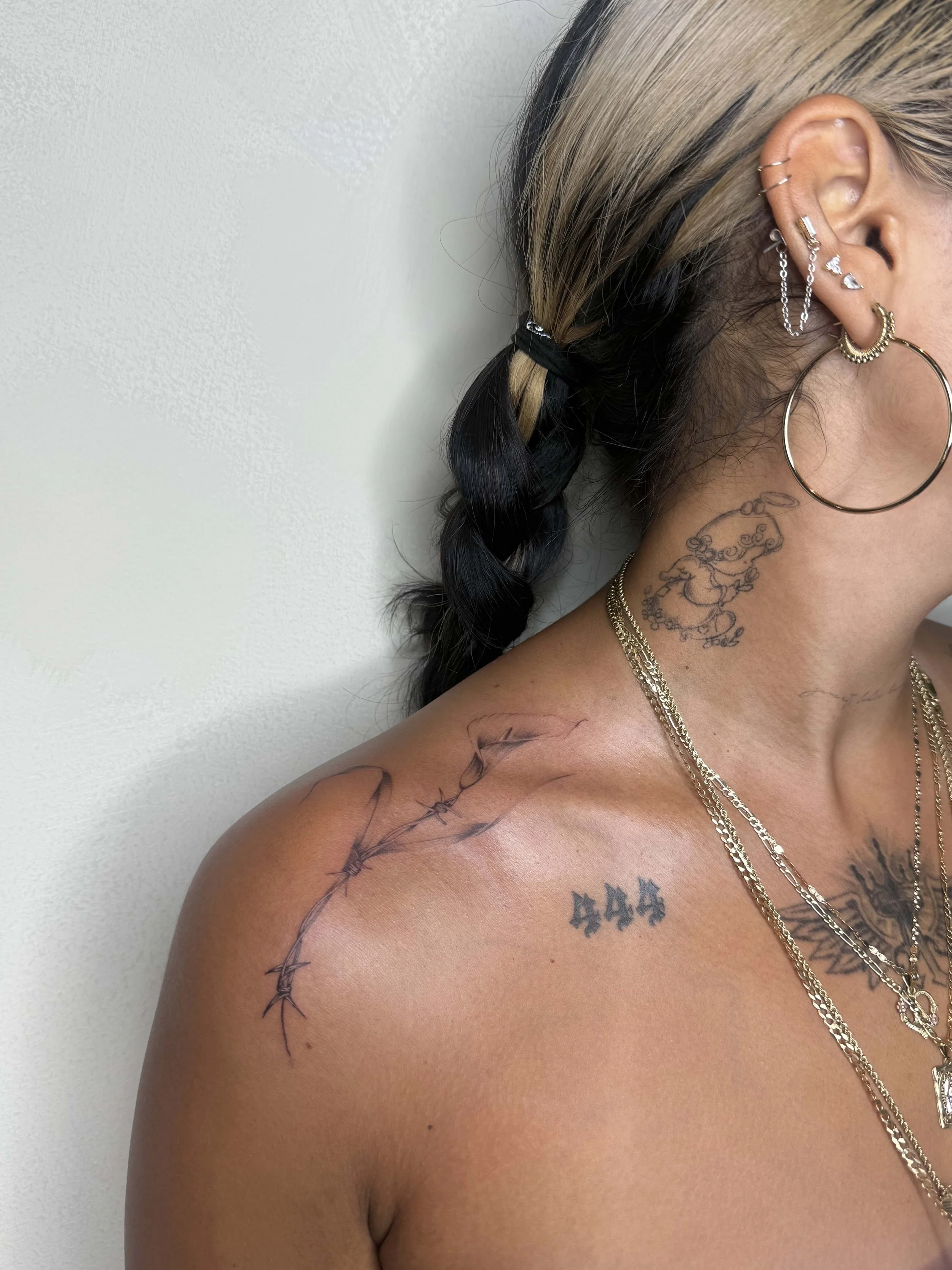 Fine-line barbed wire tattoo wrapping across the shoulder and collarbone, by Priscilla Shafighi.