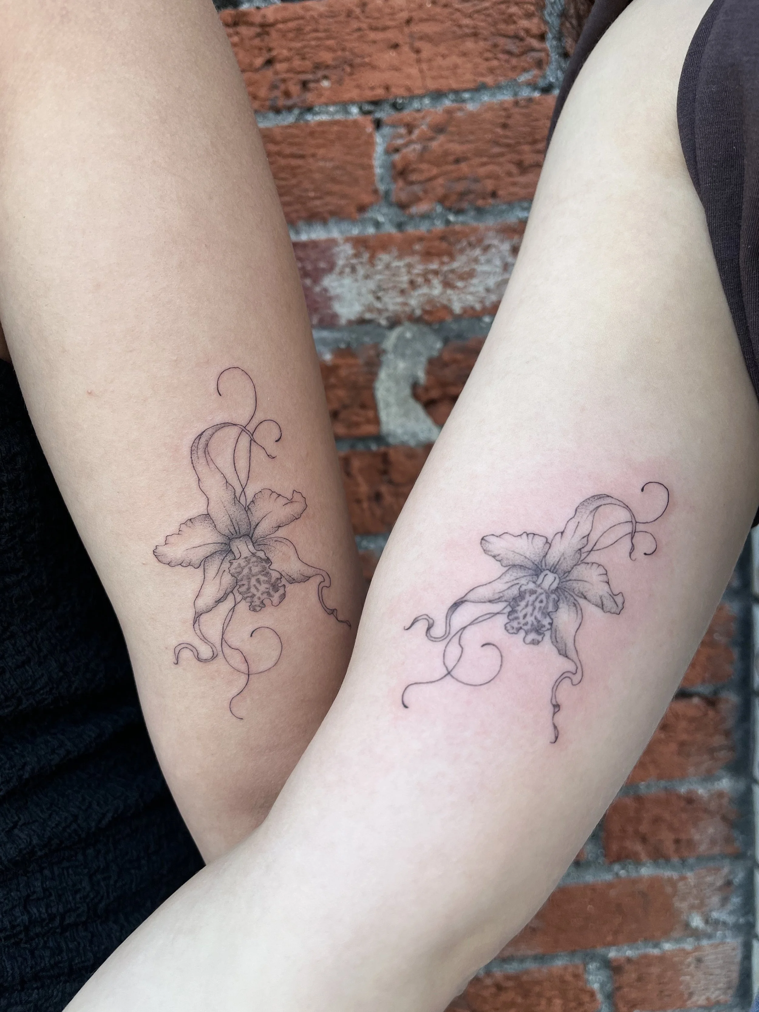 Matching fine-line floral tattoos with delicate blossoms and flowing ornamental vines, by Luna Hawke