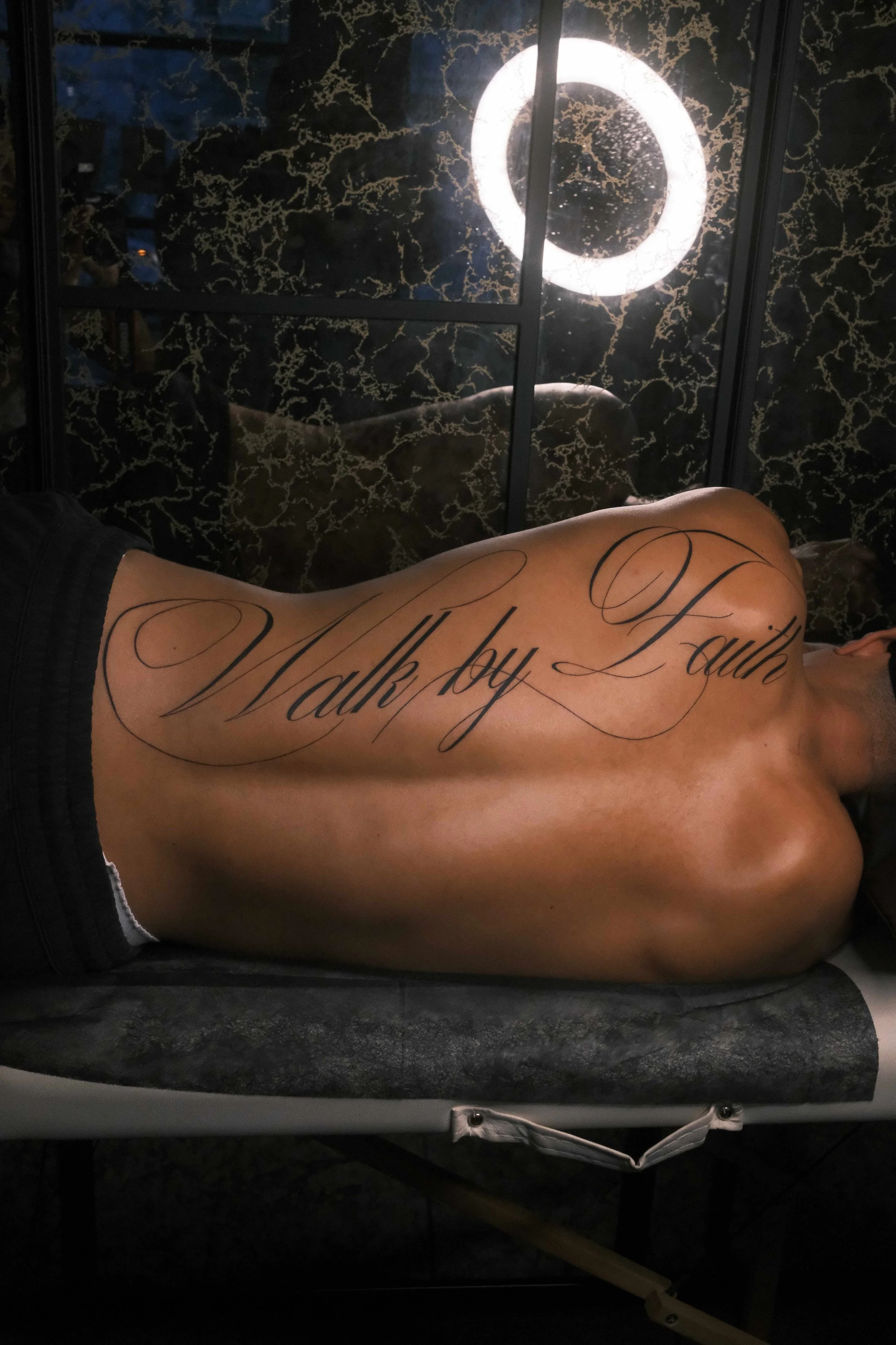 Large-scale fine-line script tattoo reading “Walk by Faith” flowing across the upper back, by Bianca Evangeline.