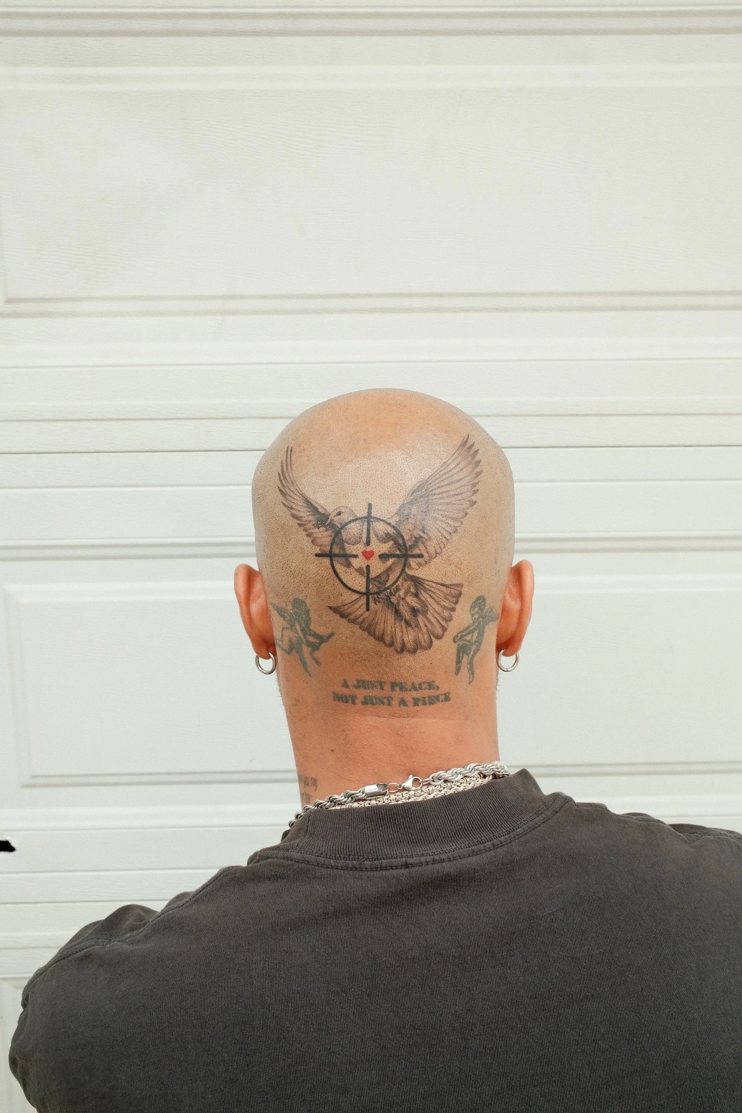 Black-and-grey dove tattoo in flight with a crosshair-style symbol and small red heart detail on the back of the head, by Bianca Evangeline.
