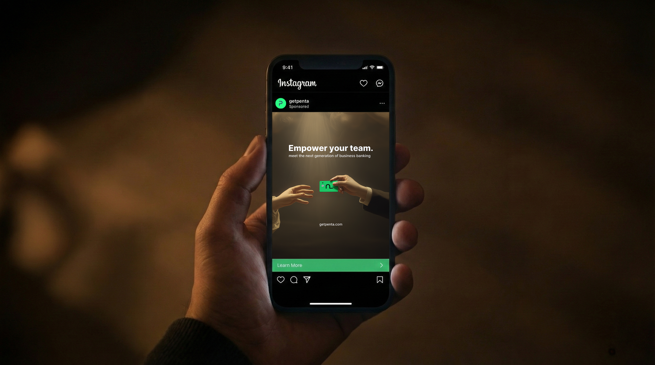 A person holding a smartphone displaying an Instagram advertisement for getpenta, featuring the phrase 'Empower your team' and a visual of two hands passing a green business card.