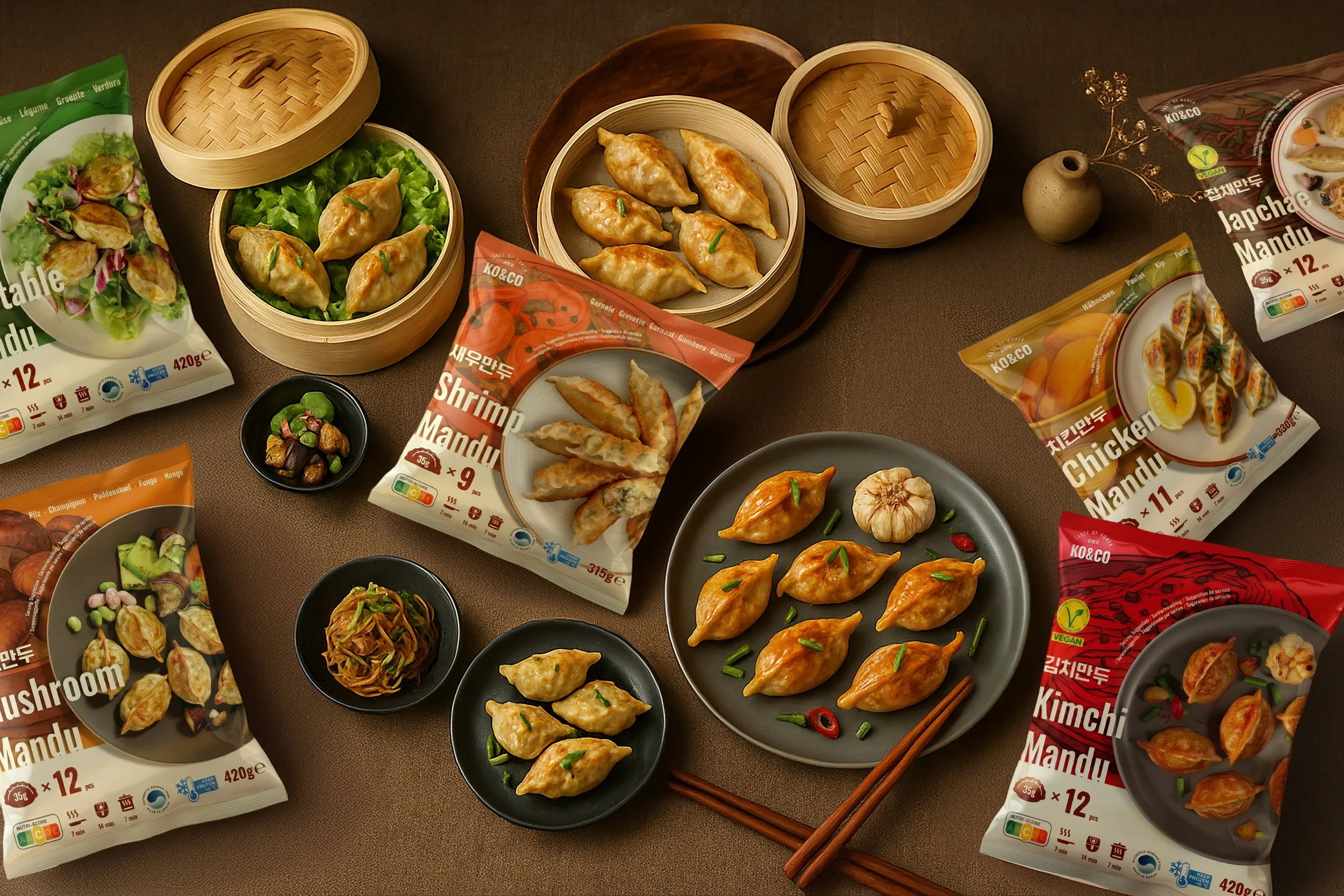 Various types of frozen mandu (Korean dumplings) and side dishes on a table, with some in bamboo steamers, bowls, and packaging.