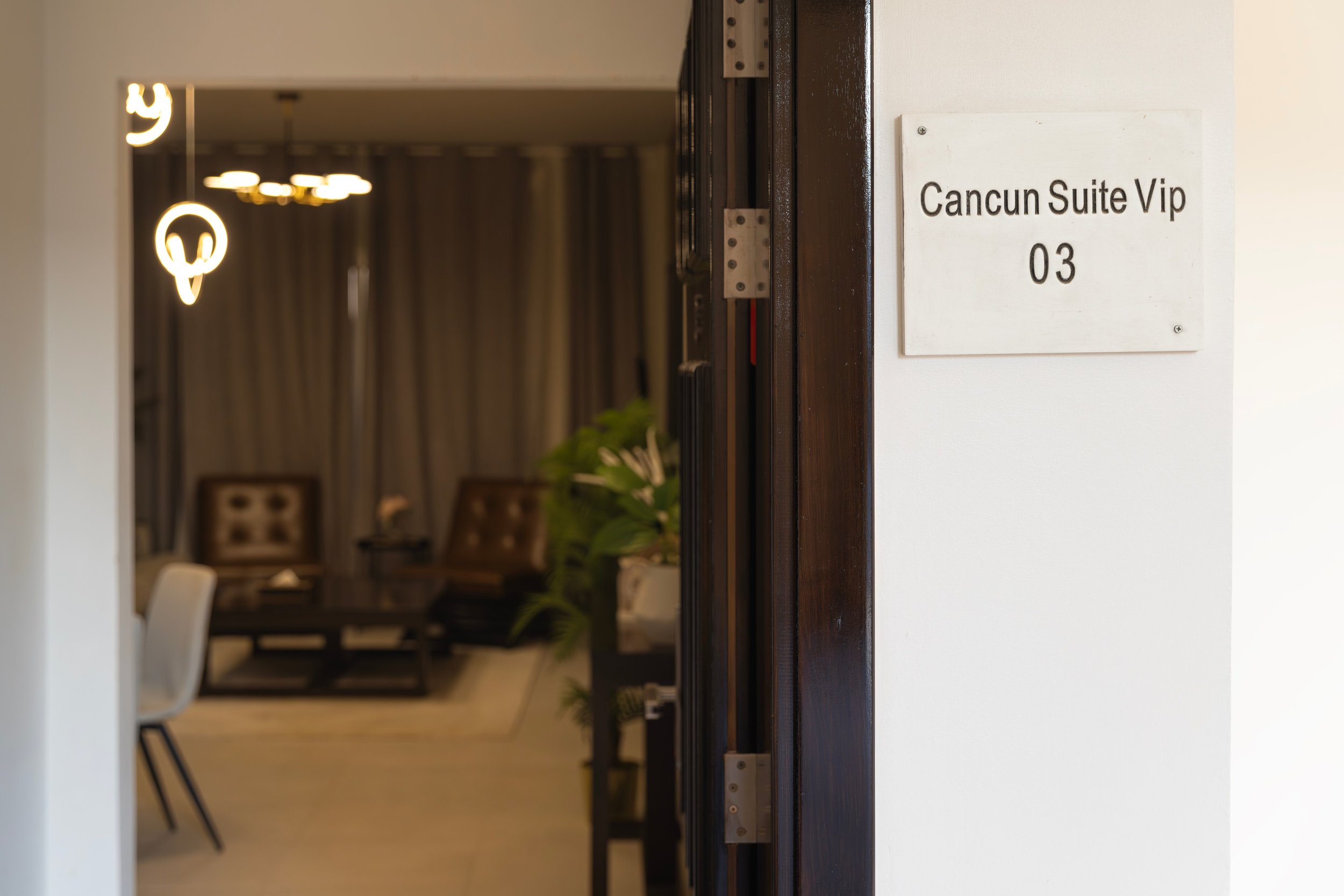Hotel room entrance with a sign that reads "Cancun Suite Vip 03", showing a glimpse of a modern, well-decorated lounge area inside.
