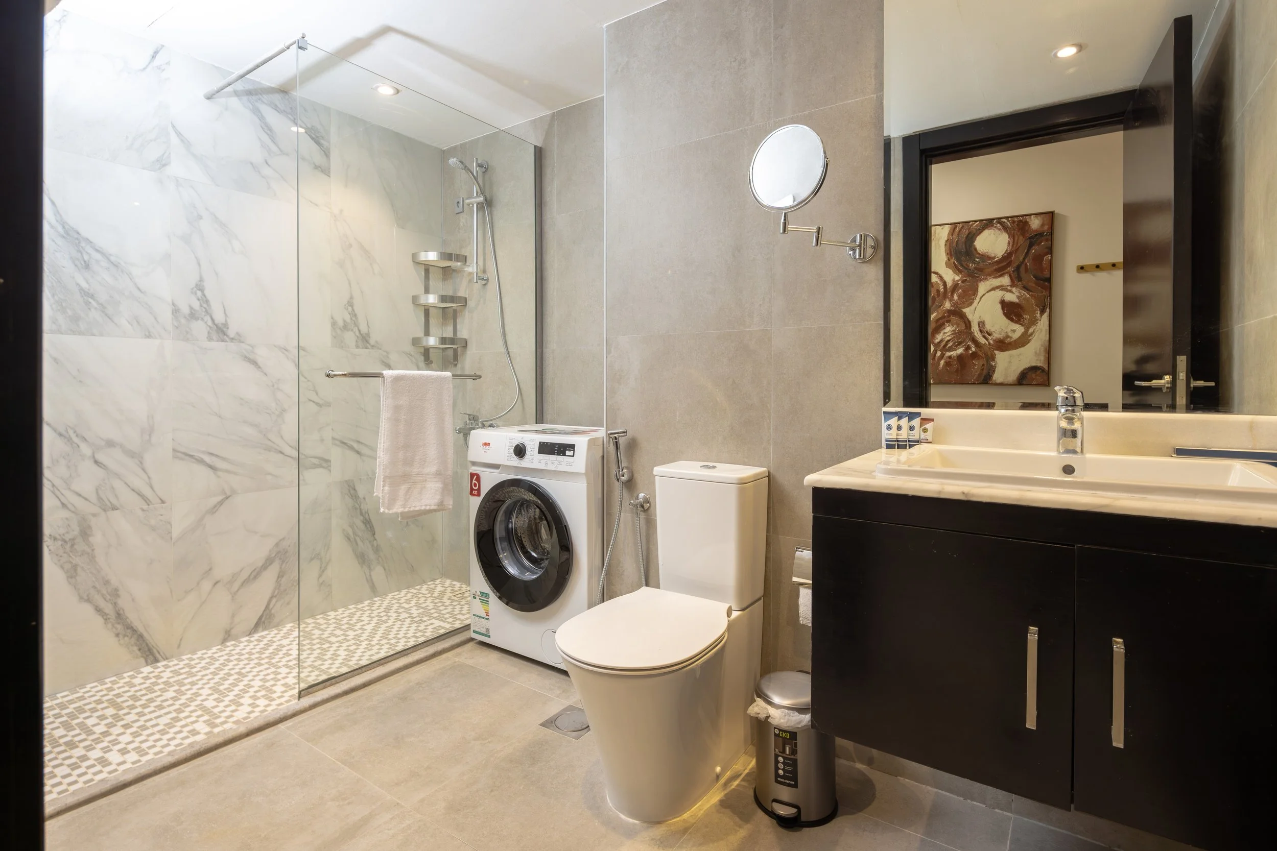 Two beds with white linens and wooden headboards, a small bedside table with a lamp, beige curtains on the side, and a rug underneath the beds.