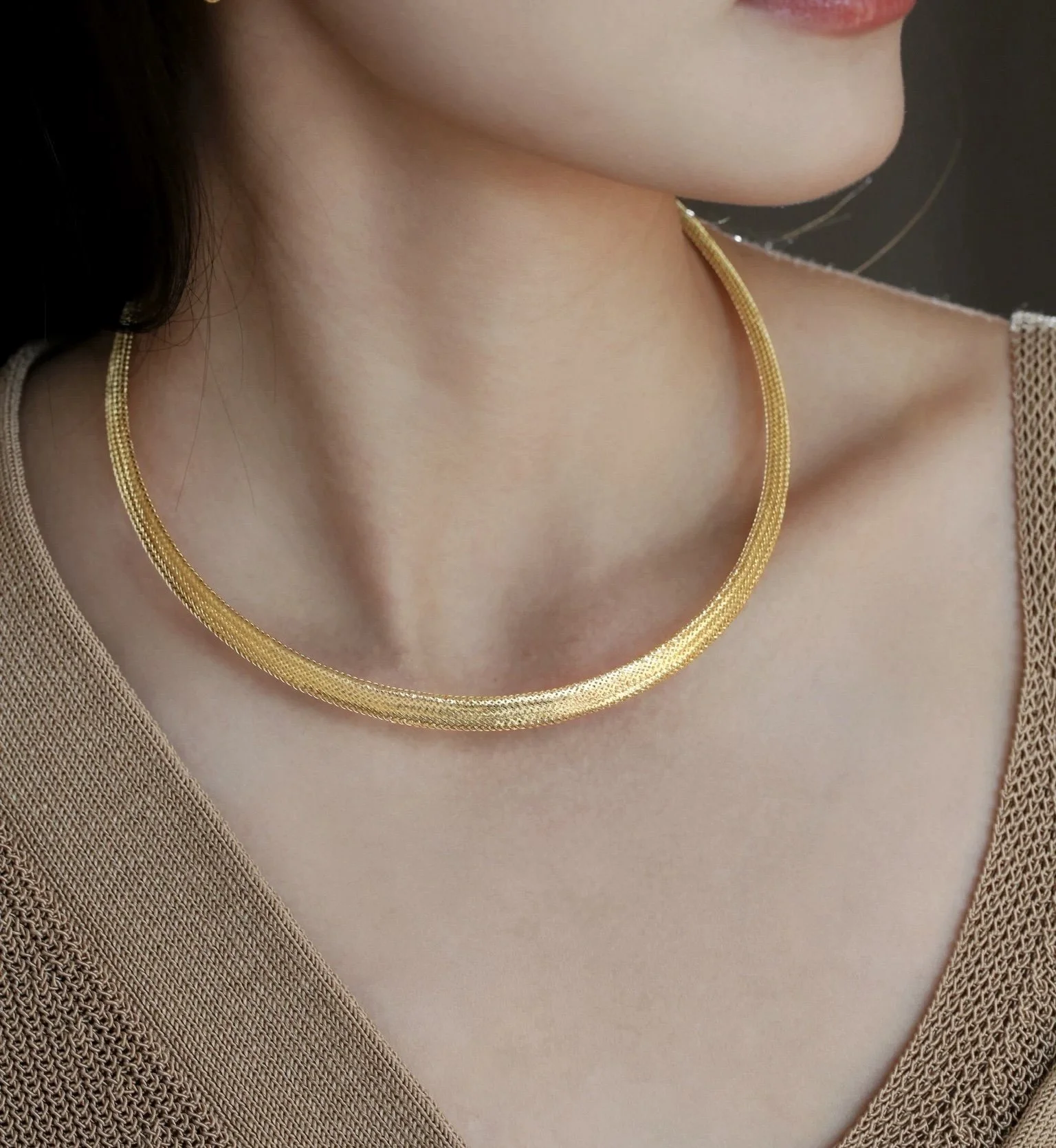 A woman wearing a gold necklace and a beige top.