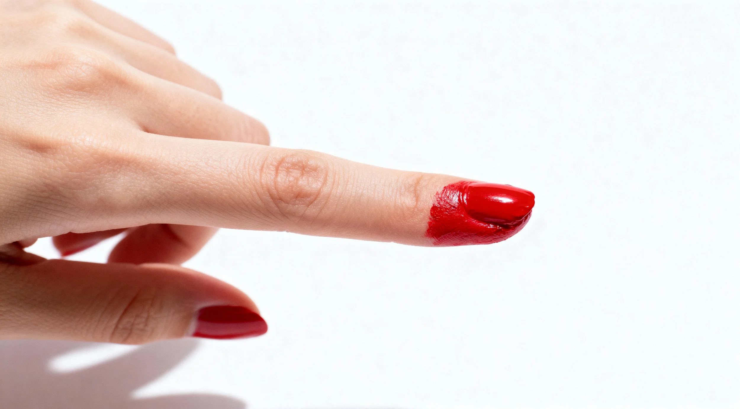 A person's index finger with red nail polish, with red paint smeared on the fingertip.