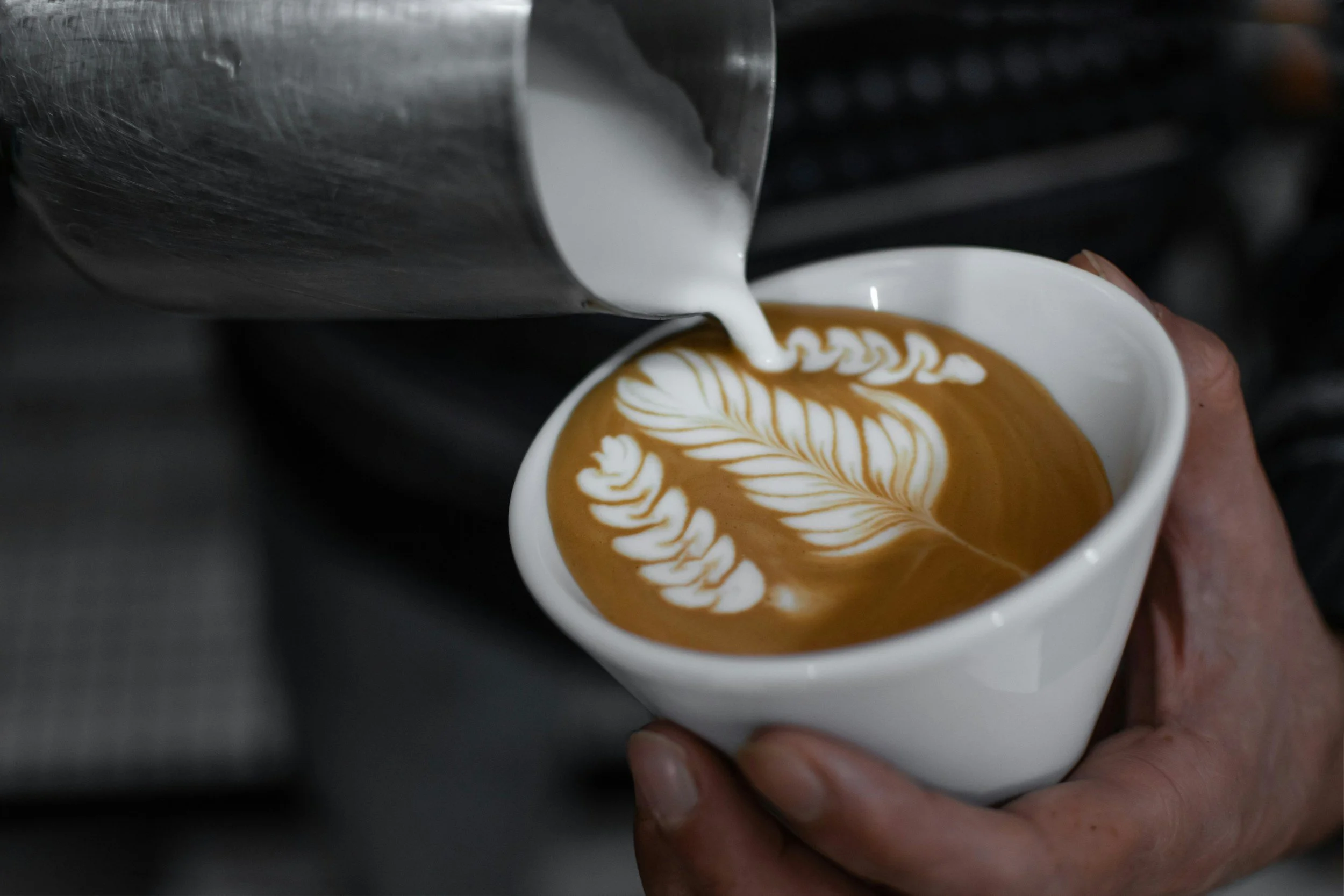 Un barista verse de la crème de lait dans un café pour créer un motif de feuille dans un latte art.