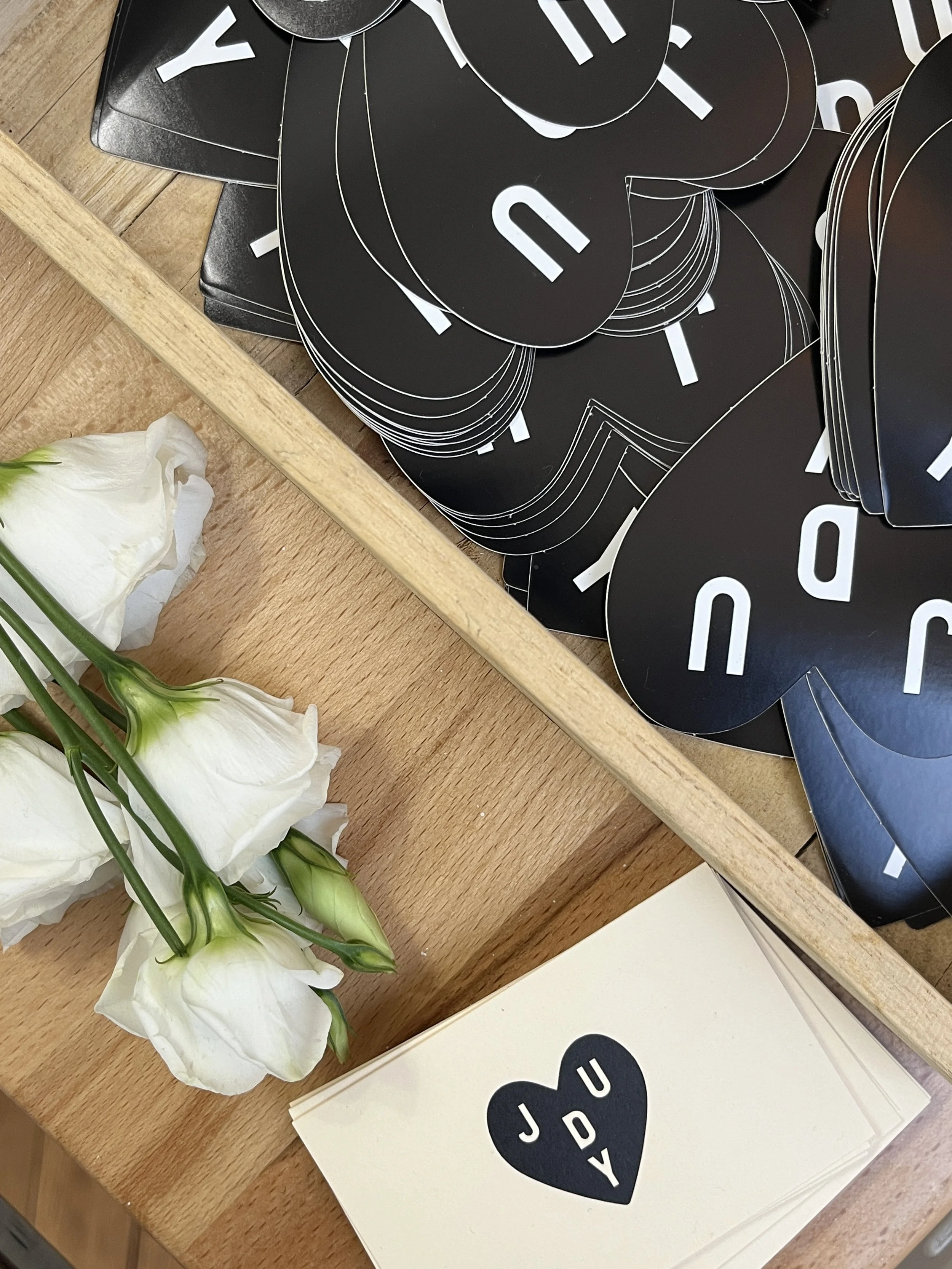 Un bouquet de fleurs blanches avec des tiges vertes, à côté d'un ensemble de cartes de vœux blanches avec un cœur noir et les lettres J et U.