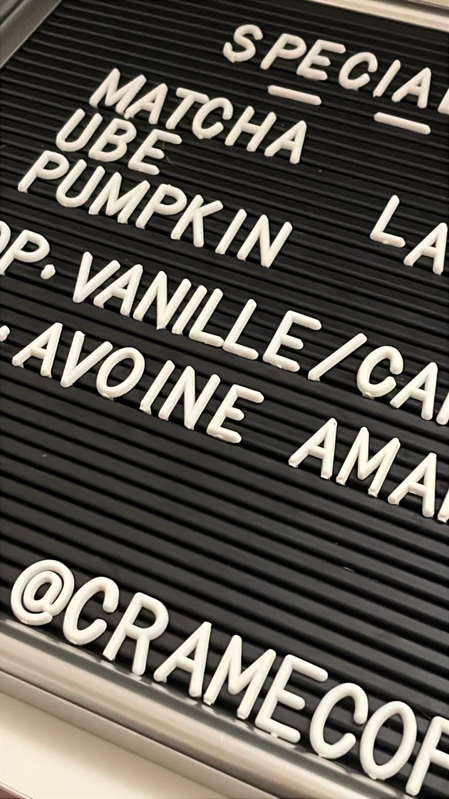 Mots en lettres blanches sur un tableau noir, listant différentes saveurs ou références : Spécial, Matcha, Ube, Pumpkin, Vanille, Café, Avoine, Amande. Inclut le texte '@CRAMECOF'
