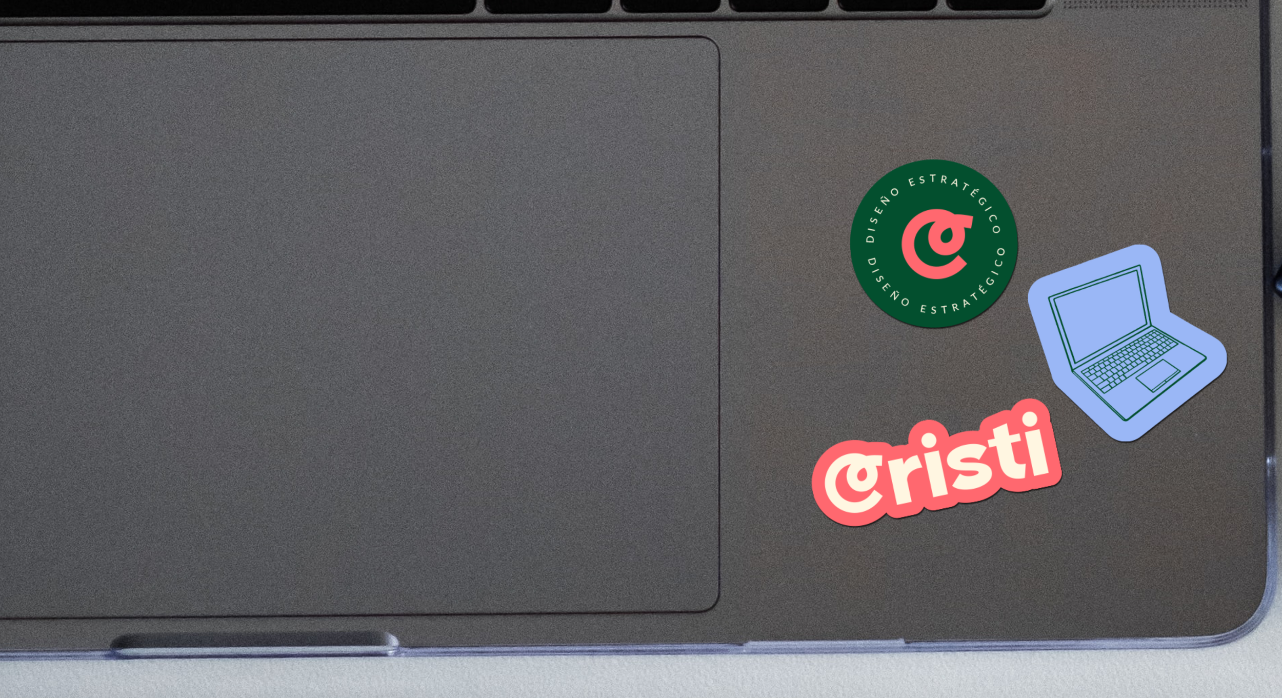 Laptop with three colorful stickers: a green circle with a pink logo and text in Spanish, a blue outline of a laptop, and red text '@cristi' with a pink and white outline.