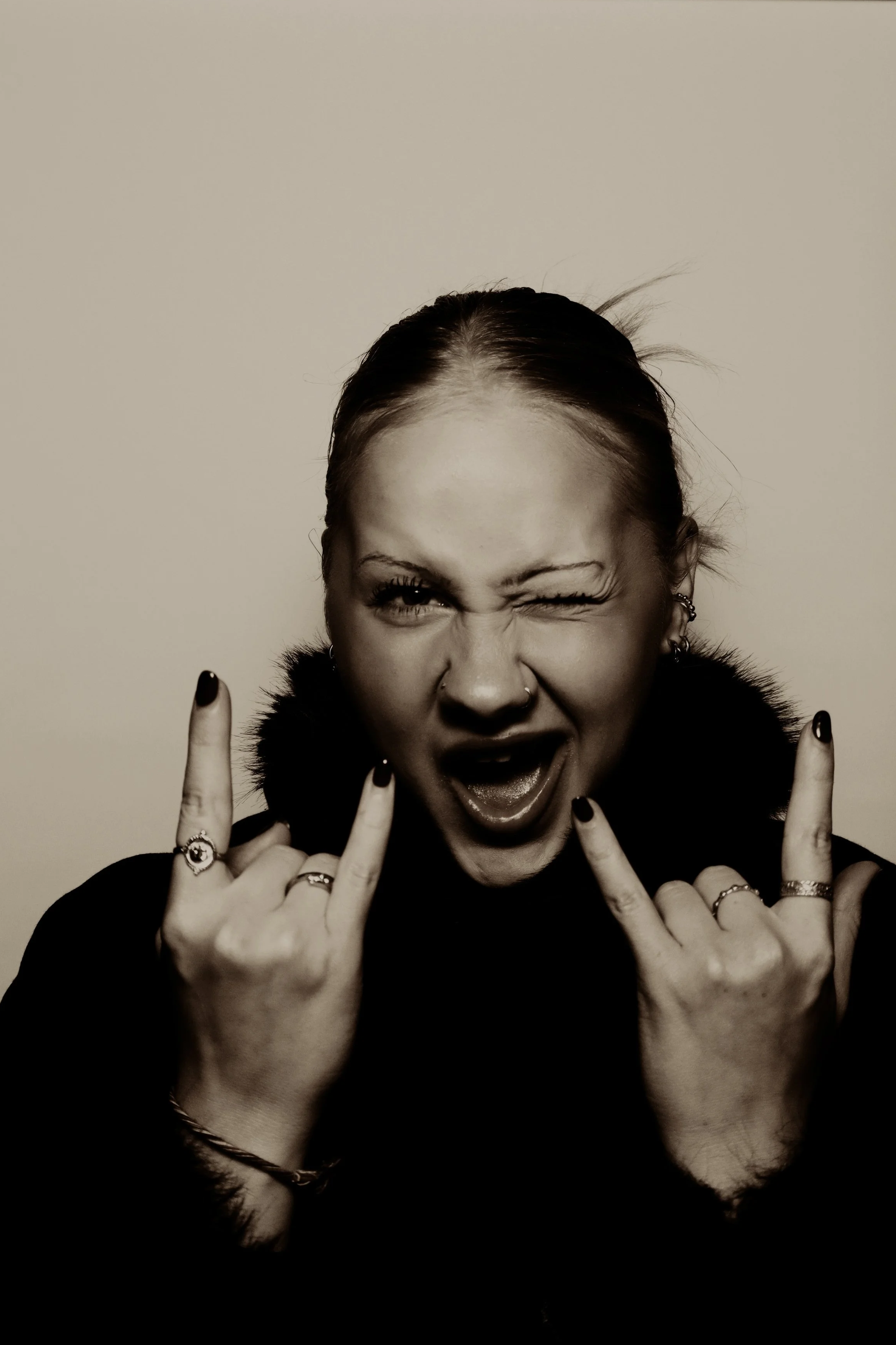 Nuori nainen tekee rokkikäden symbolin, huutaa tai nauraa iloisesti, mustavalkoinen kuva.