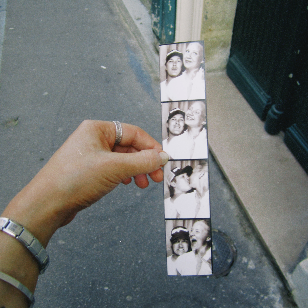 Kuva hihasta, jolla on ranneranneke ja sormus, joka pitää valokuvasankkiloa, jossa on neljä mustavalkoista valokuvaa pariskunnasta, jotka ovat pusertuneet kaksi kauniin hymyn kanssa.