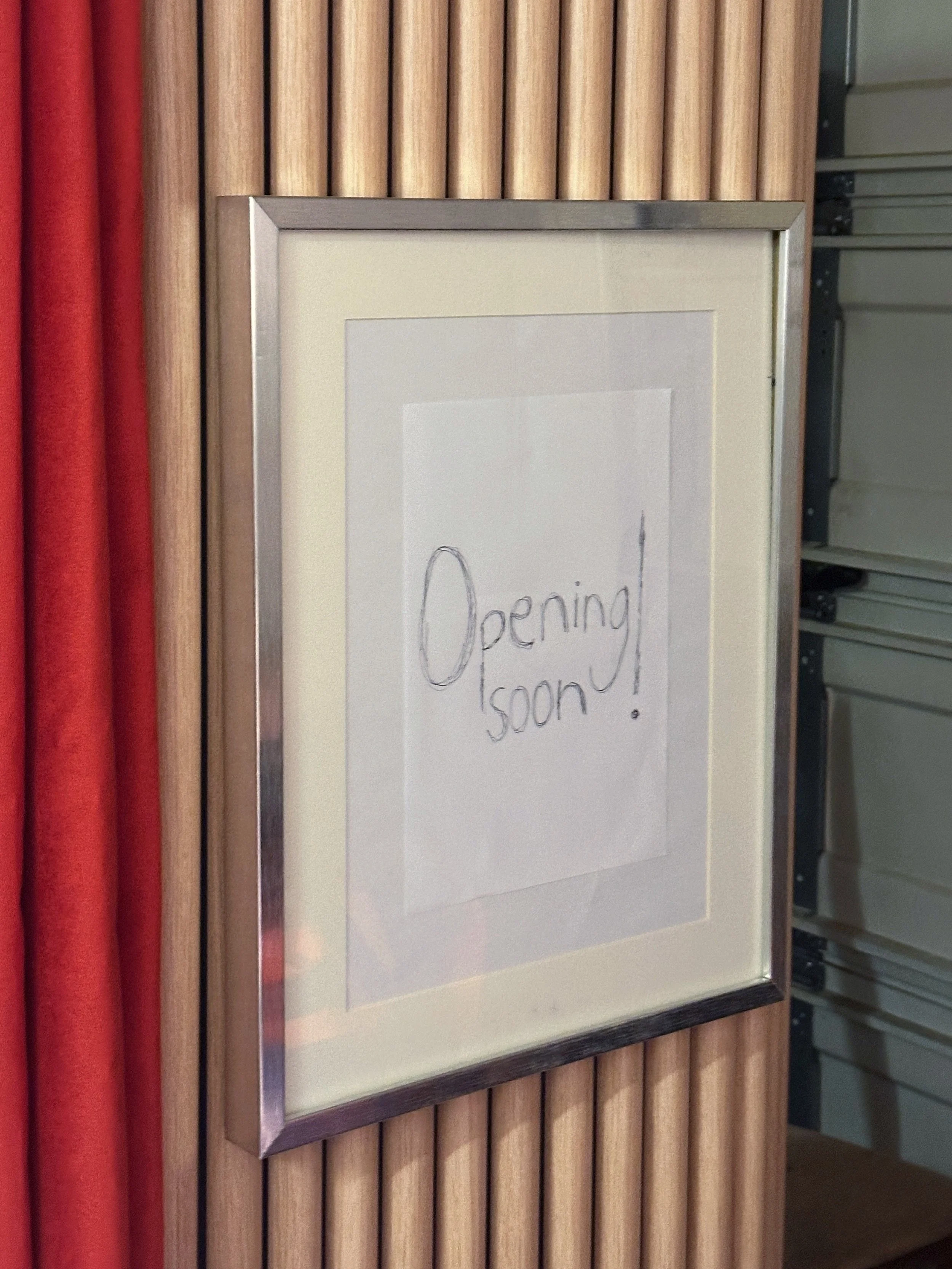 Valkoinen taulu, jossa lukee käsin 'Opening soon!'.