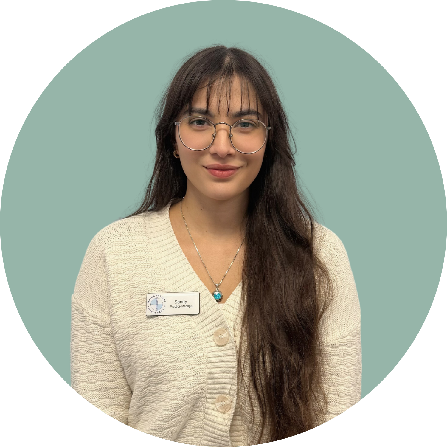 A young woman with long brown hair, glasses, and a beige cardigan, smiling, wearing a name tag that reads Sandy Practice Manager, against a light green background.