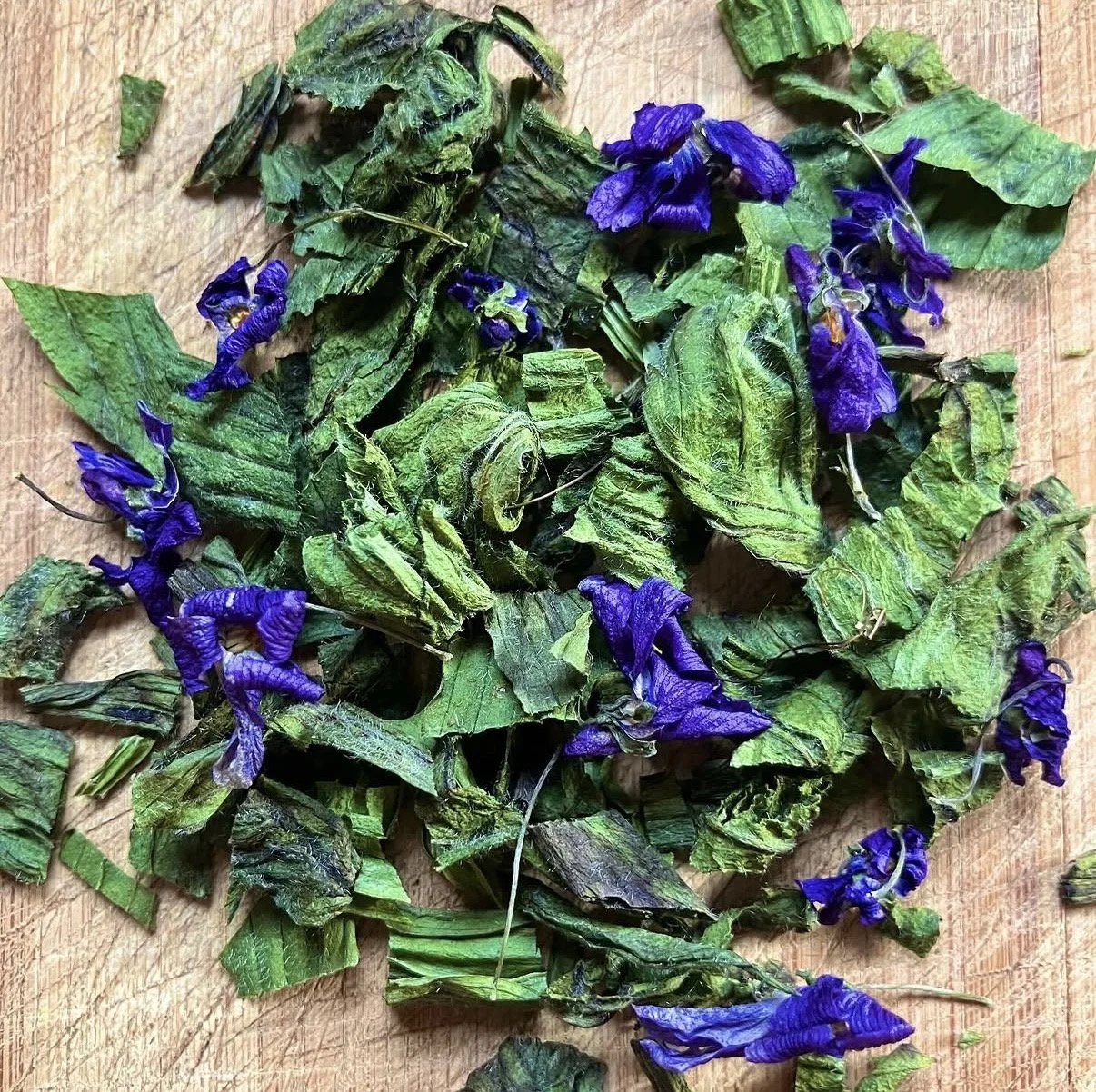 Dried green leaves and purple flowers on a wooden surface.