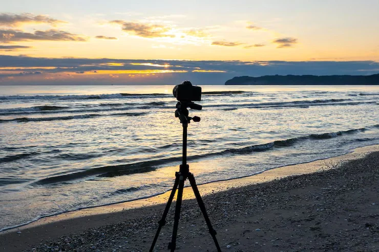 Sarasota Motor Club - Exotic Car Rental Sarasota Florida - A camera on a tripod set up on a beach during sunset, with the ocean and a distant landmass in the background.