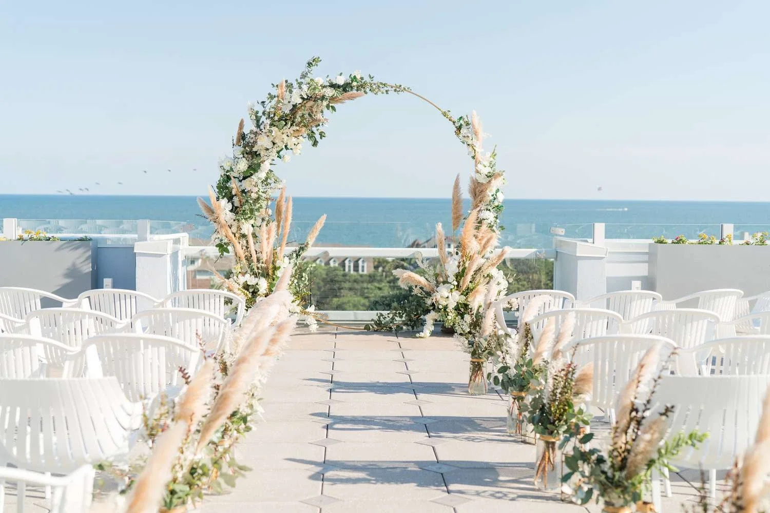 Sarasota Motor Club - Luxury Car Sarasota - Outdoor wedding ceremony setup on a rooftop with white chairs, floral arch, and ocean view.