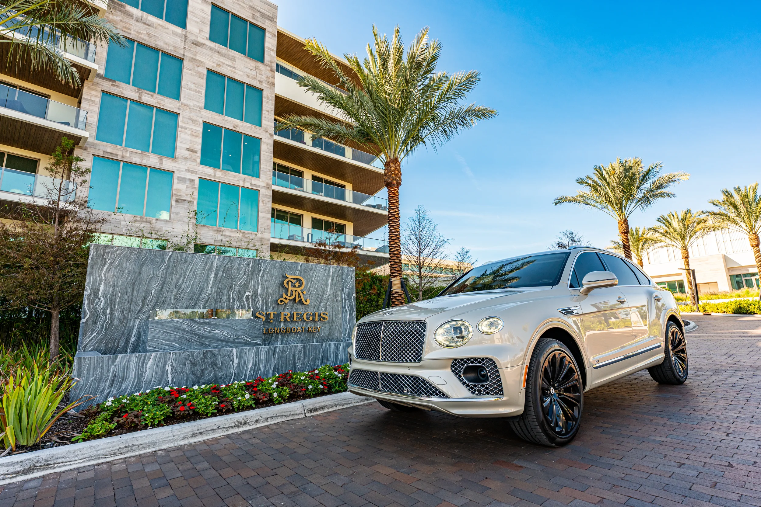 Sarasota Motor Club - private driver wedding Sarasota - Luxury white SUV parked near the entrance of the St. Regis Longboat Key hotel, with modern hotel building, palm trees, and a sunny blue sky in the background.
