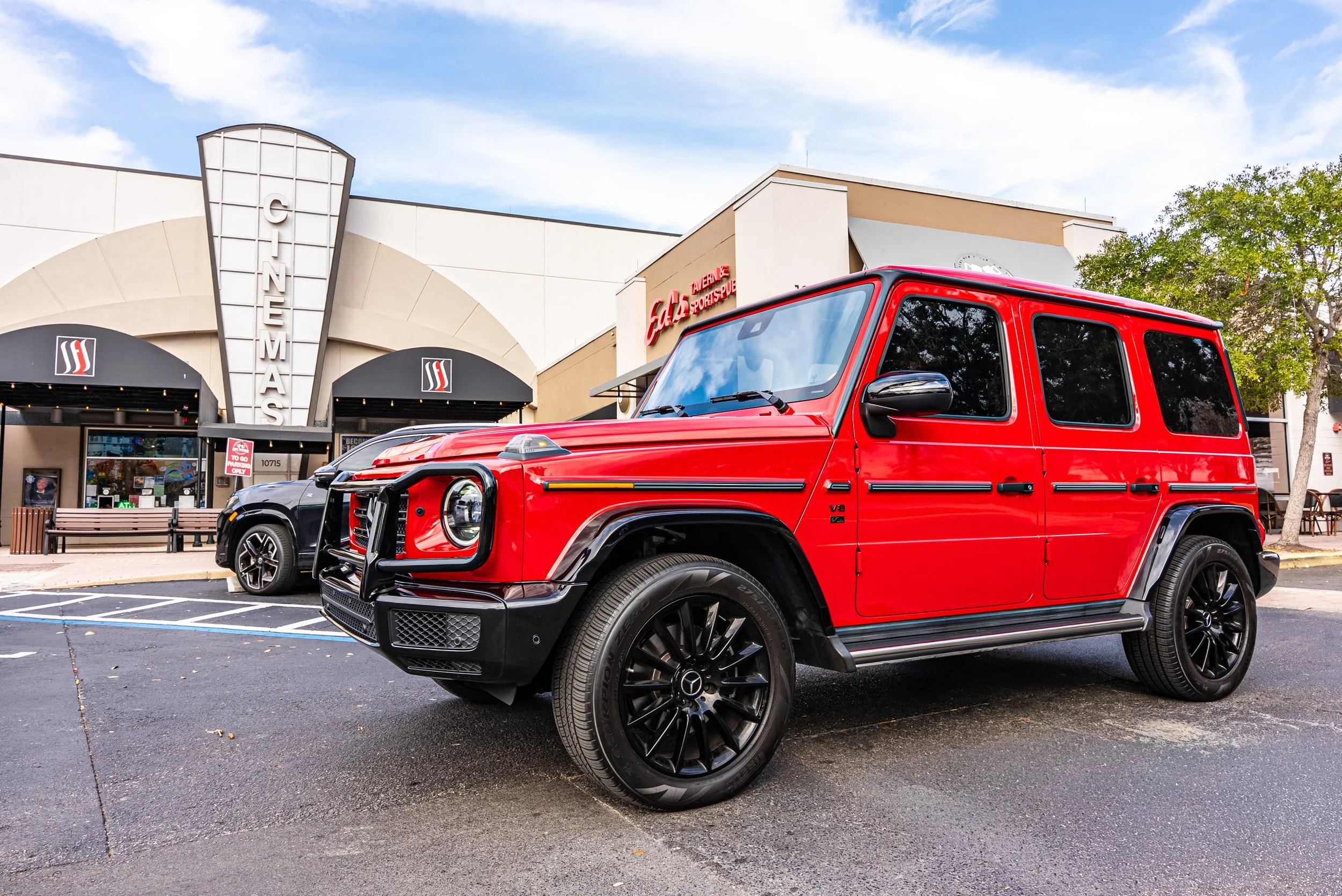 Sarasota Motor Club - premium car service sarasota - A red Mercedes-Benz G-Class SUV parked outside a cinema with a building in the background.