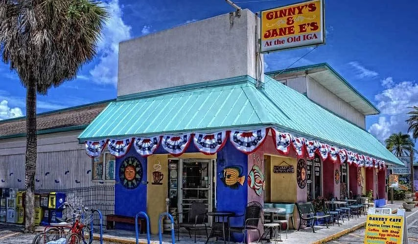 Sarasota Motor Club - Premium Car Service Sarasota - Exterior of Ginny's & Jane E's bakery with a blue awning decorated with red, white, and blue bunting, outdoor seating, and a sign indicating it's a bakery cafe.