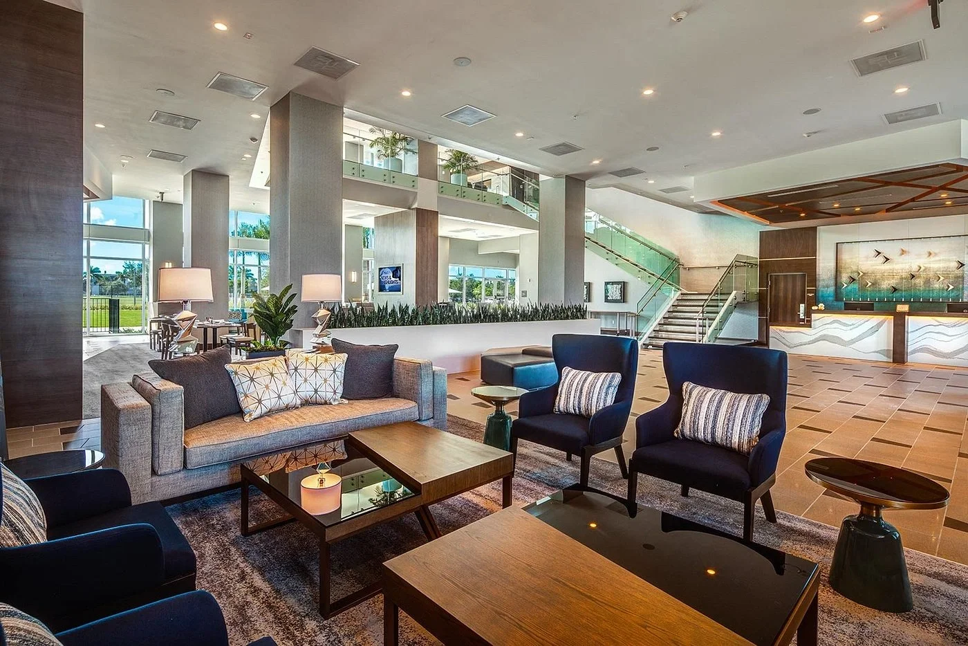 Sarasota Motor Club - Exotic Car Rental Sarasota Florida - Modern hotel lobby with seating area, various chairs and a sofa, coffee tables, large windows, staircase, reception desk, and decorative art.