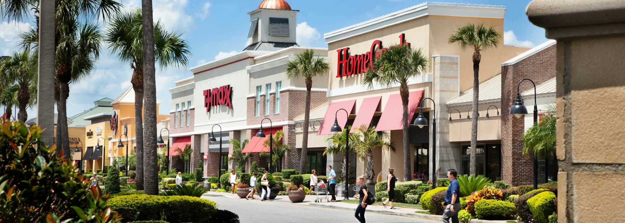 Sarasota Motor Club - Sarasota Luxury Car Rental - Retail shopping area with a HomeGoods store, palm trees, people shopping and walking, and storefronts with red awnings.