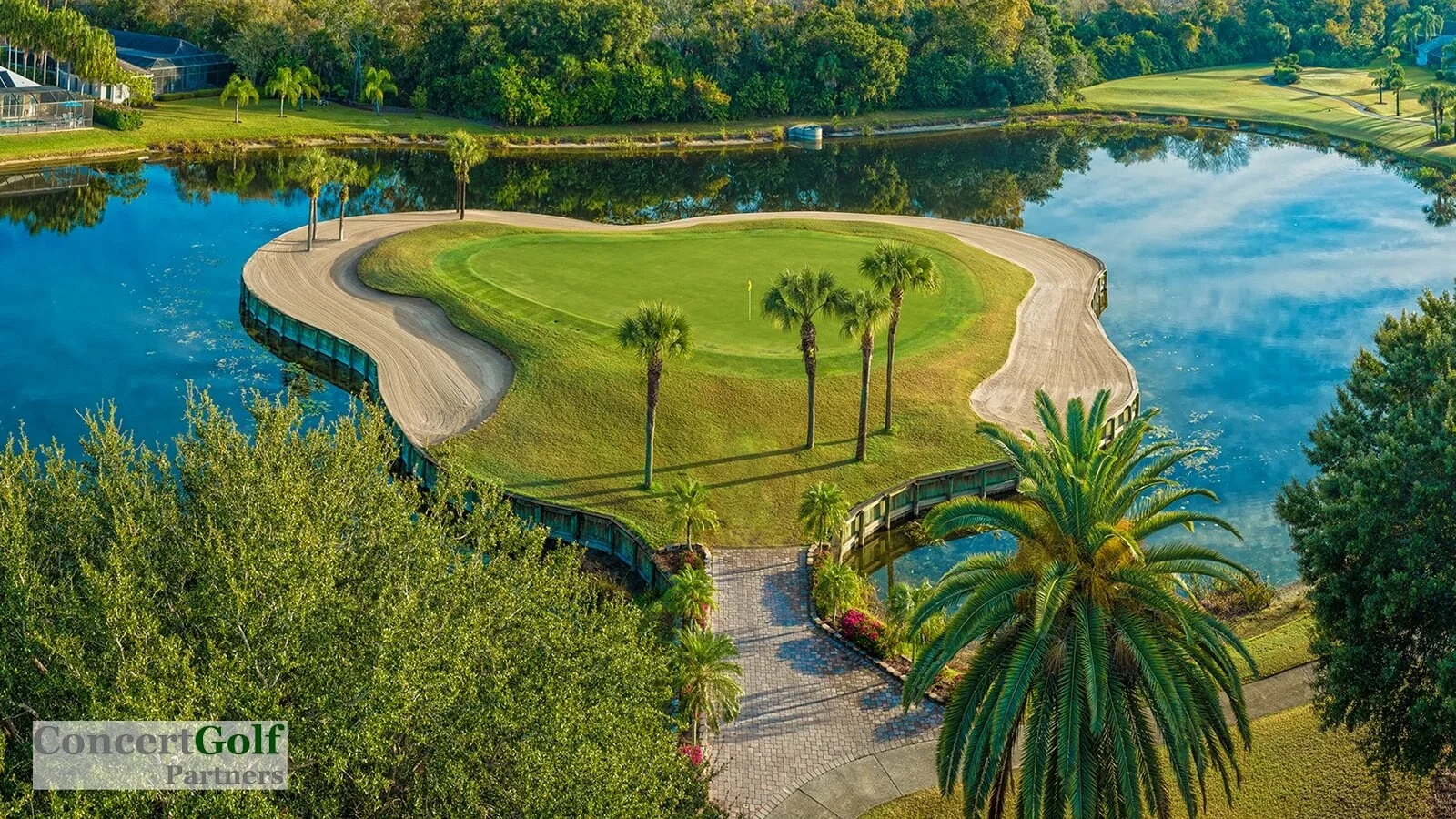 Sarasota Motor Club - Premium Car Service Sarasota - A golf course island green surrounded by water, with a pathway and palm trees at the entrance, and lush green trees in the background.