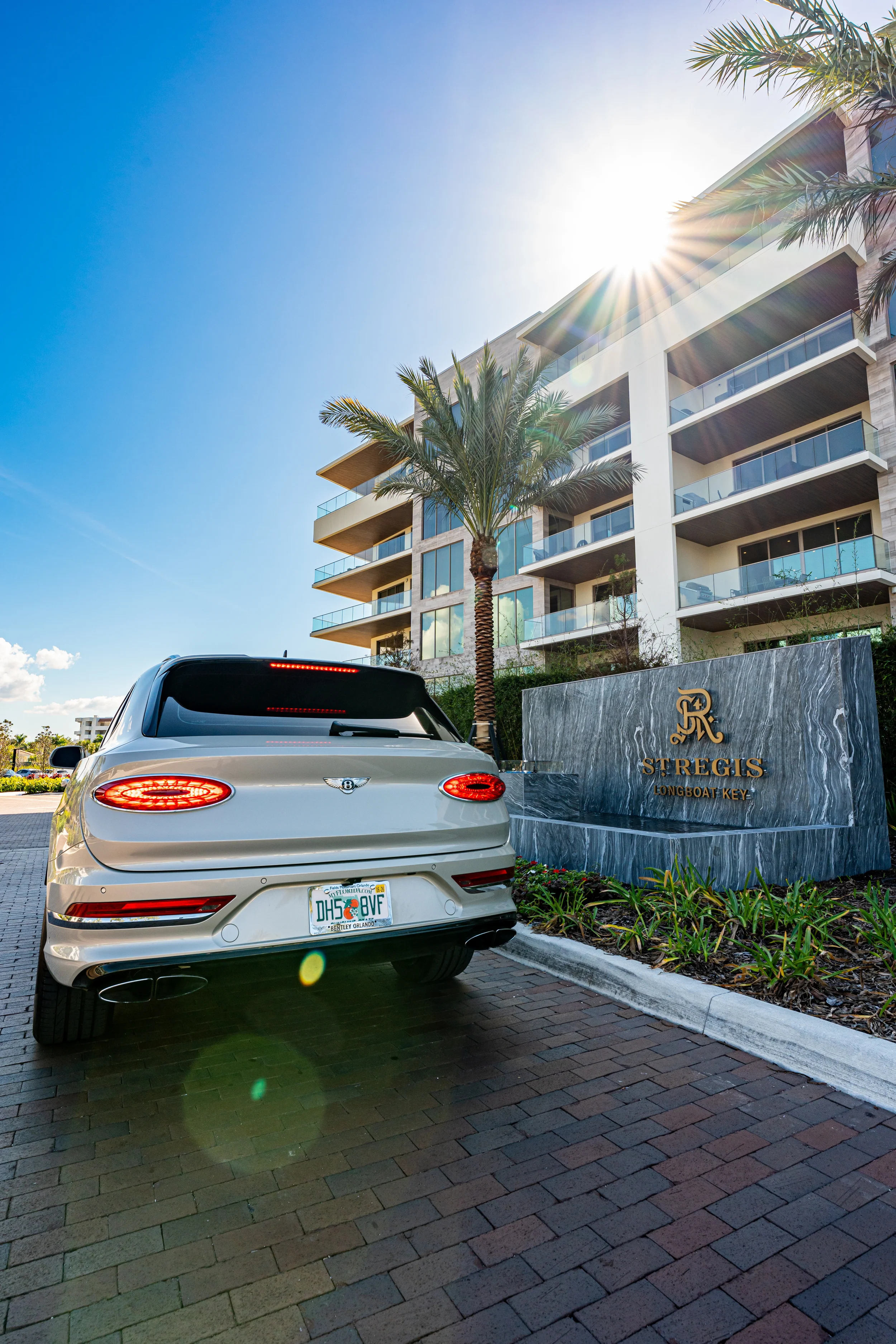 Sarasota Motor Club - siesta key exotic car rental - A luxury white Bentley car parked outside the St. Regis hotel in Longboat Key, Florida, with modern apartment buildings and palm trees in the background on a sunny day.