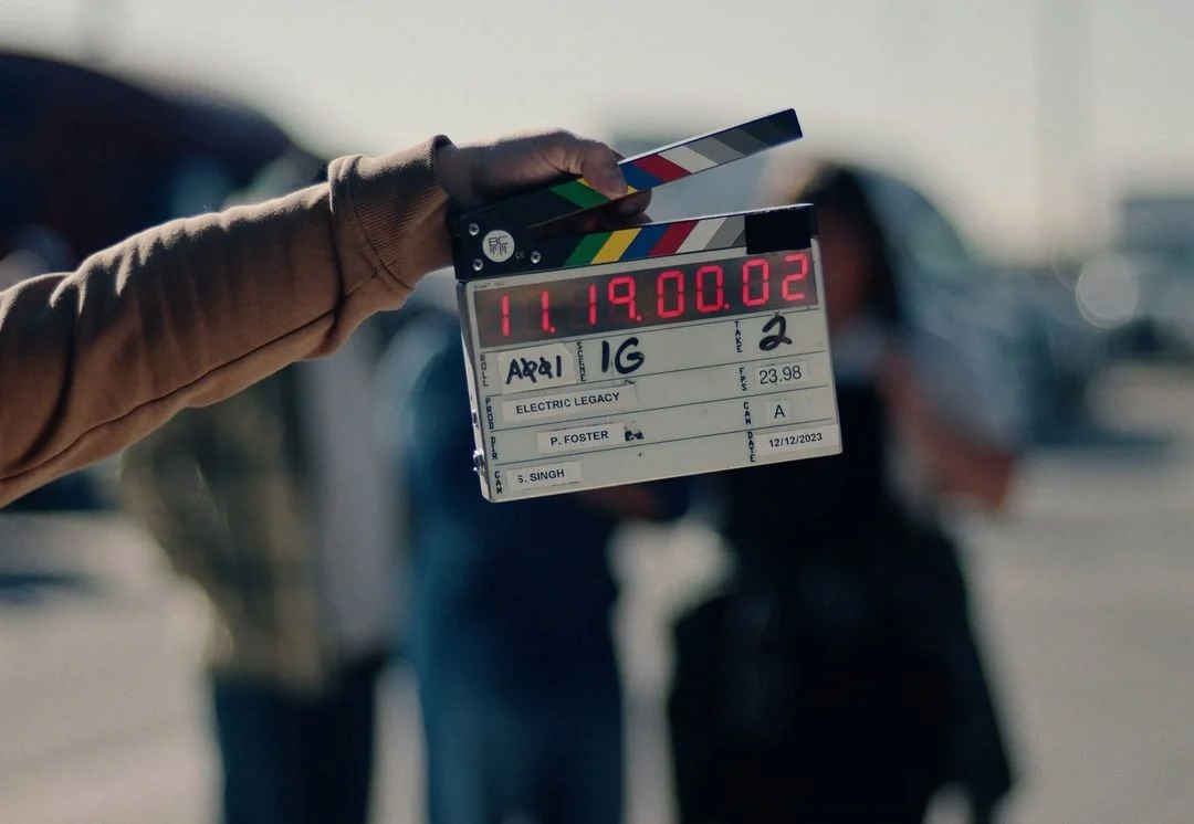 Sarasota Motor Club - Exotic Car Rental Sarasota Florida - Hand holding a film slate or clapperboard with a blurred background of parked cars and people.
