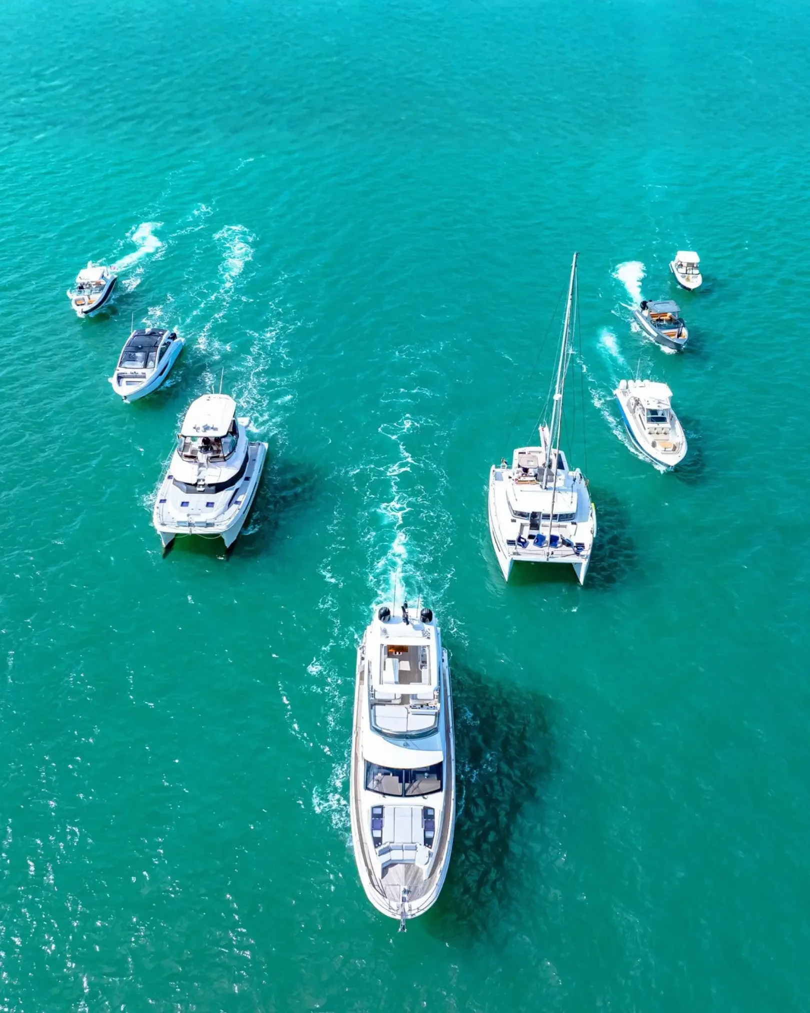 Aerial view of several boats, including yachts and small motorboats, cruising on turquoise ocean water.