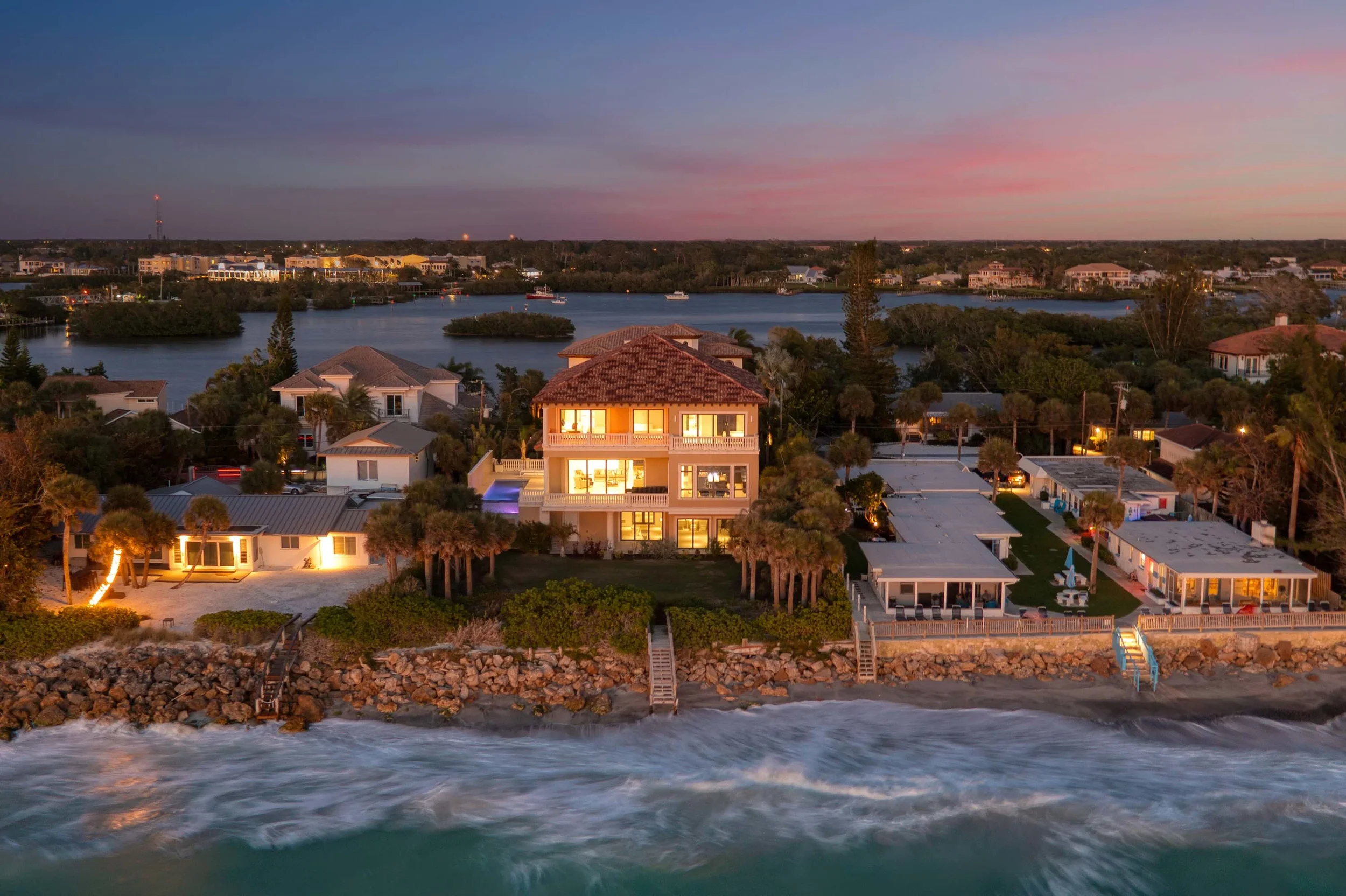 Sarasota Motor Club - Exotic Car Consignment Sarasota - Aerial view of houses by a shoreline at sunset, with water, boats, and a colorful sky.