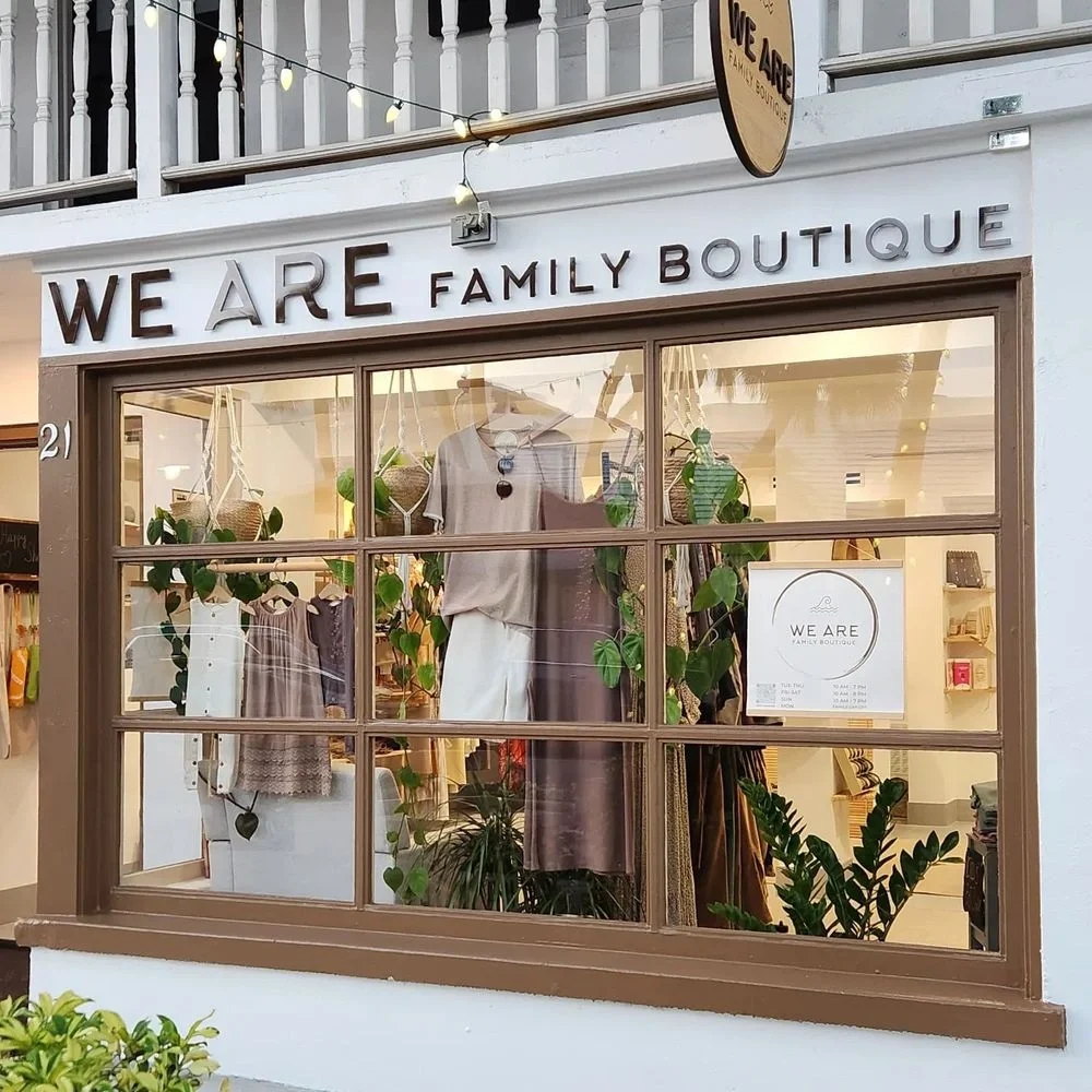 Sarasota Motor Club - Premium Car Service Sarasota - Front window of a boutique clothing store named "We Are Family Boutique" displaying clothing inside and decorated with plants.