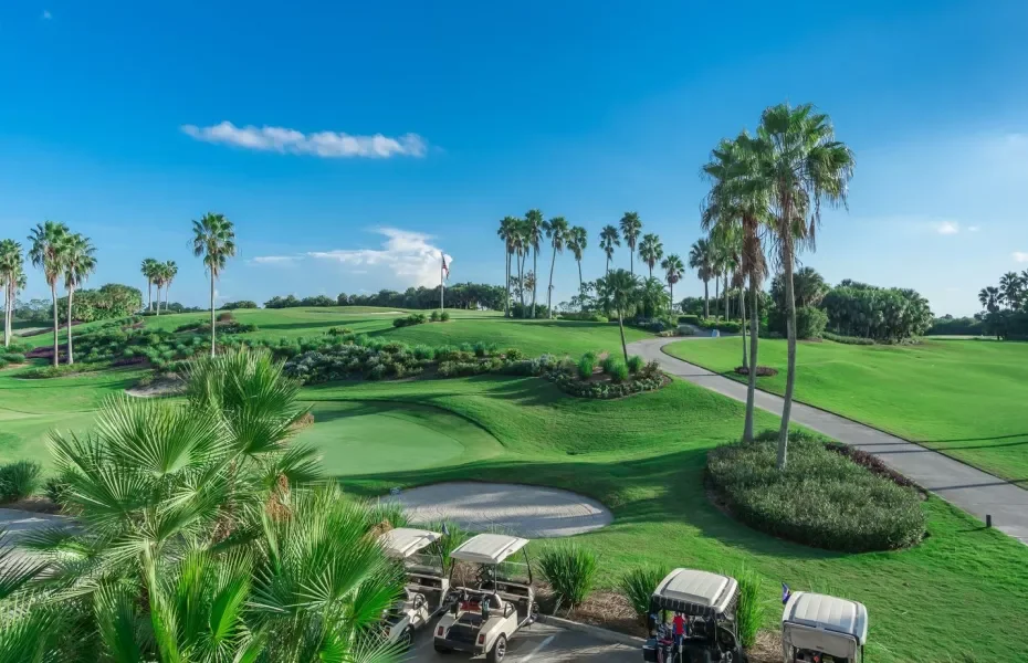 Sarasota Motor Club - Premium Car Service Sarasota - A scenic view of a golf course with green fairways, palm trees, a paved cart path, and a few golf carts in the foreground, under a clear blue sky.