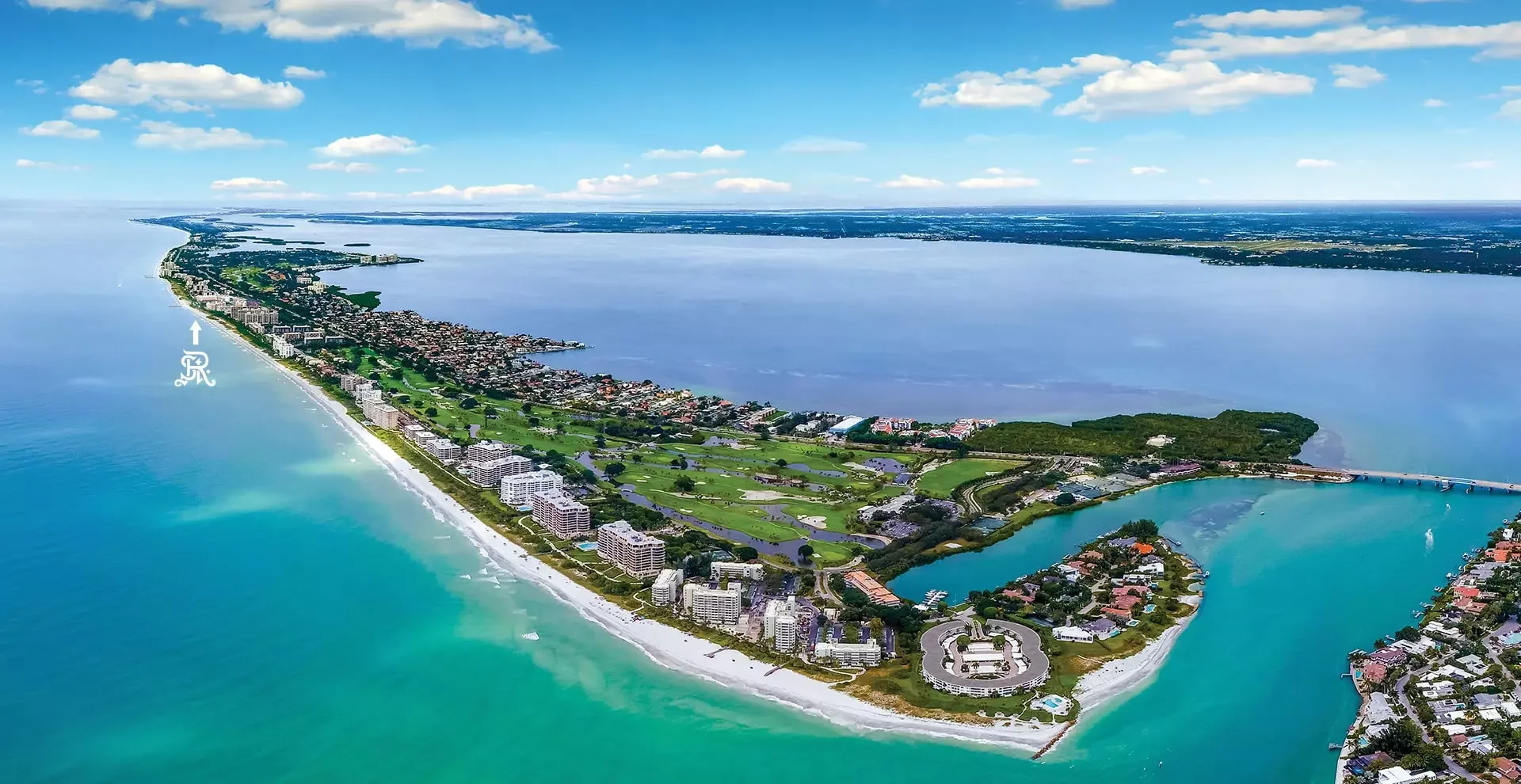Sarasota Motor Club - Sports Car Rental Sarasota FL - Aerial view of a coastal town with beaches, buildings, green parks, and a river, next to a large body of water under a partly cloudy sky.